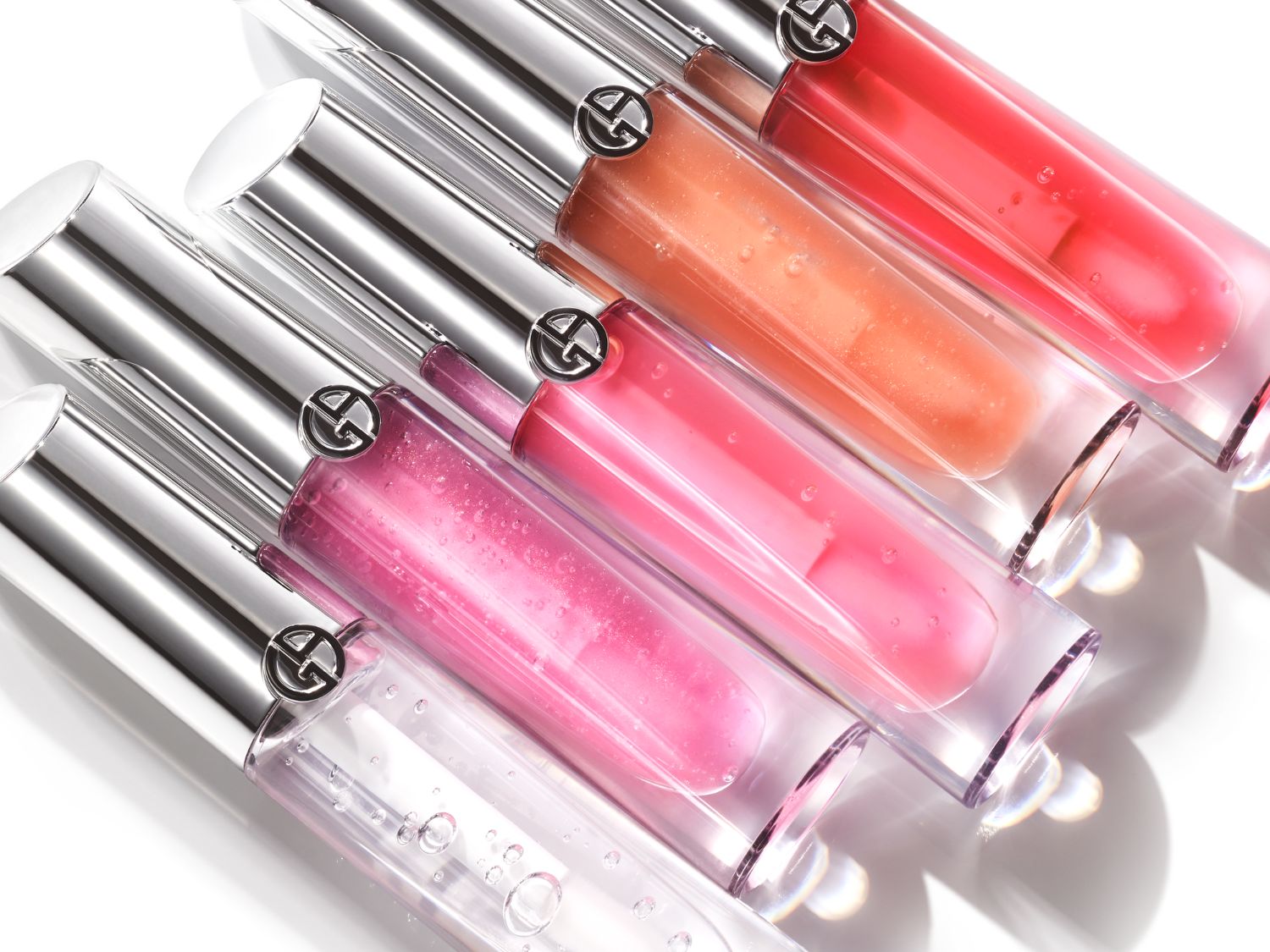 Řada lesků na rty Giorgio Armani s průhledným obalem a stříbrným víčkem, které odhalují různé odstíny od čiré přes růžovou, broskvovou až po červenou.