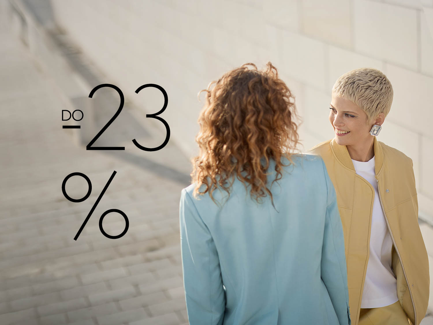 Dwie kobiety ubrane w pastelowe marynarki stoją na schodach, a obok nich widnieje napis -23%, co sugeruje promocję.
