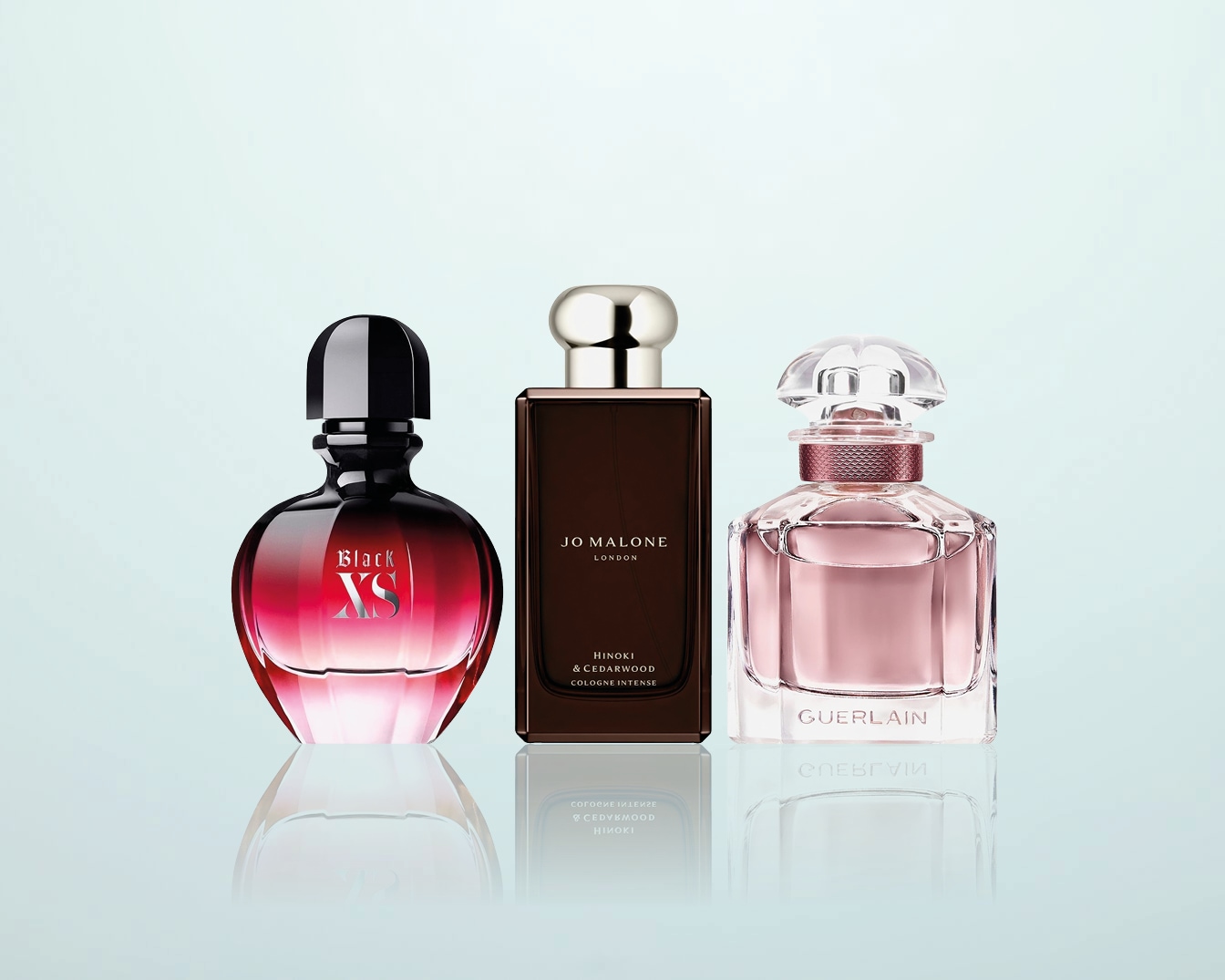 Drie parfumflessen staan op een rij: Black XS met een rood-zwarte gradiënt, Jo Malone Hinoki & Cedarwood in een bruine flacon, en Guerlain in een zachtroze tint.