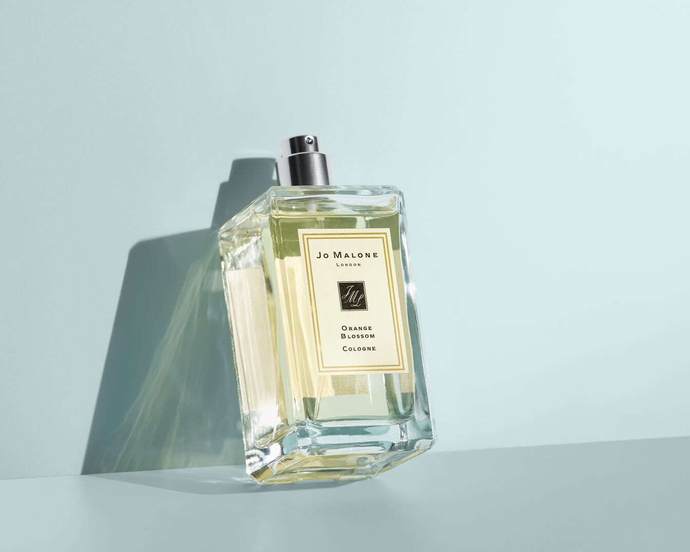 Een heldere, vierkante fles Jo Malone London Orange Blossom Cologne met een zilveren dop staat op een lichtblauwe achtergrond.