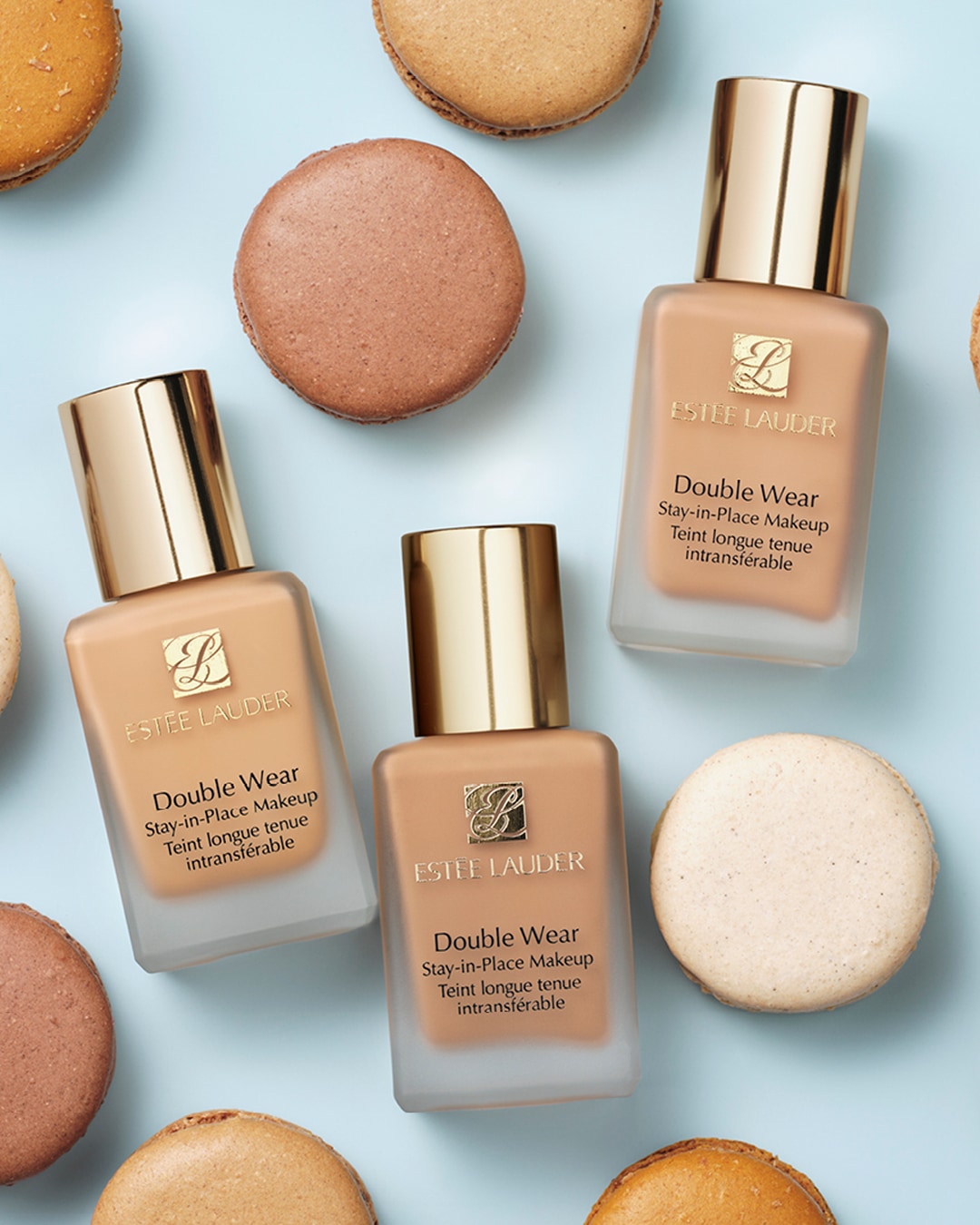 Trois flacons de fond de teint Estée Lauder Double Wear entourés de macarons colorés, offrant une couvrance longue tenue pour un teint impeccable.