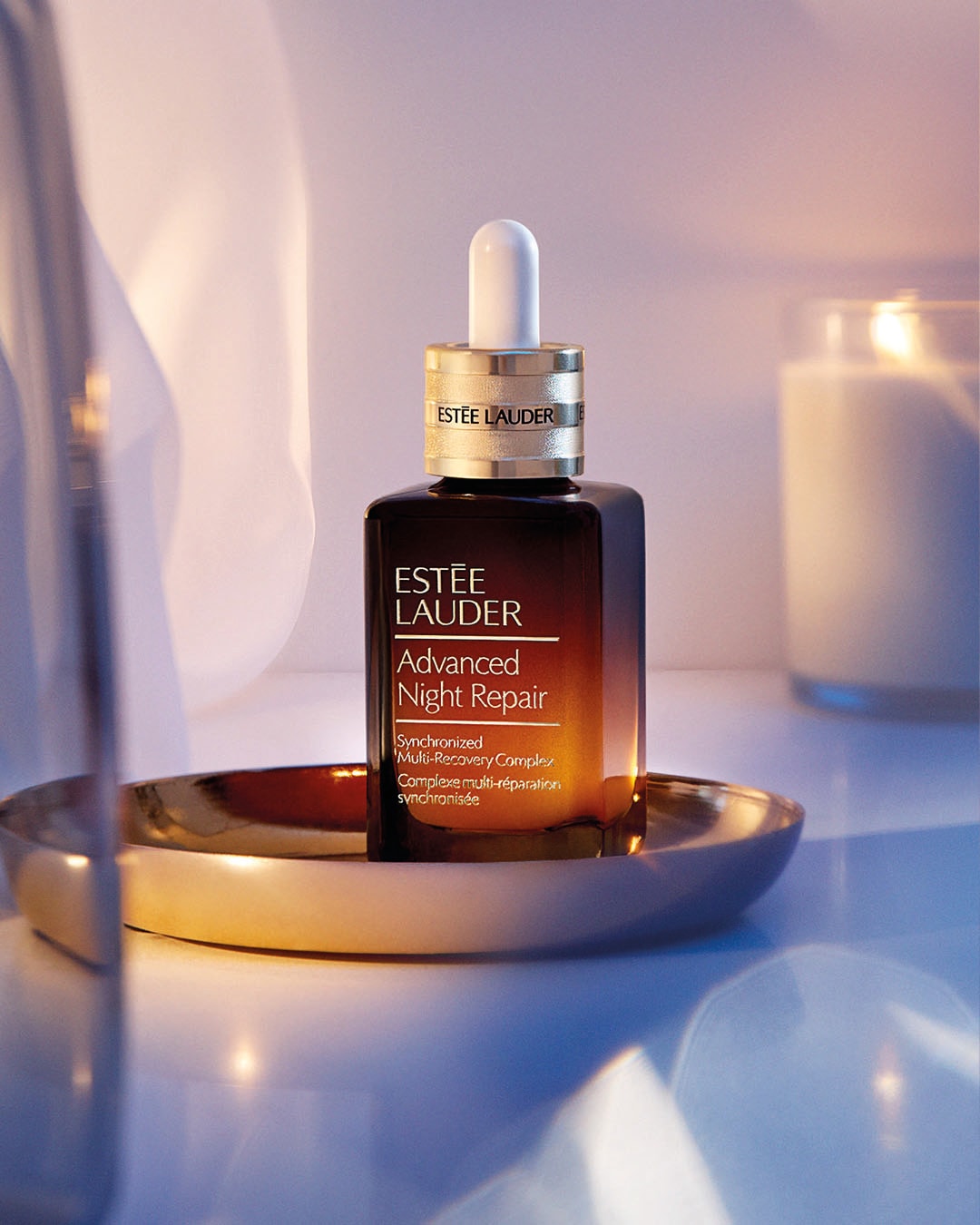 Flacon carré brun dégradé d'Estée Lauder Advanced Night Repair avec pipette blanche, sur un plateau doré, promettant un complexe multi-réparation synchronisée pour une peau revitalisée.