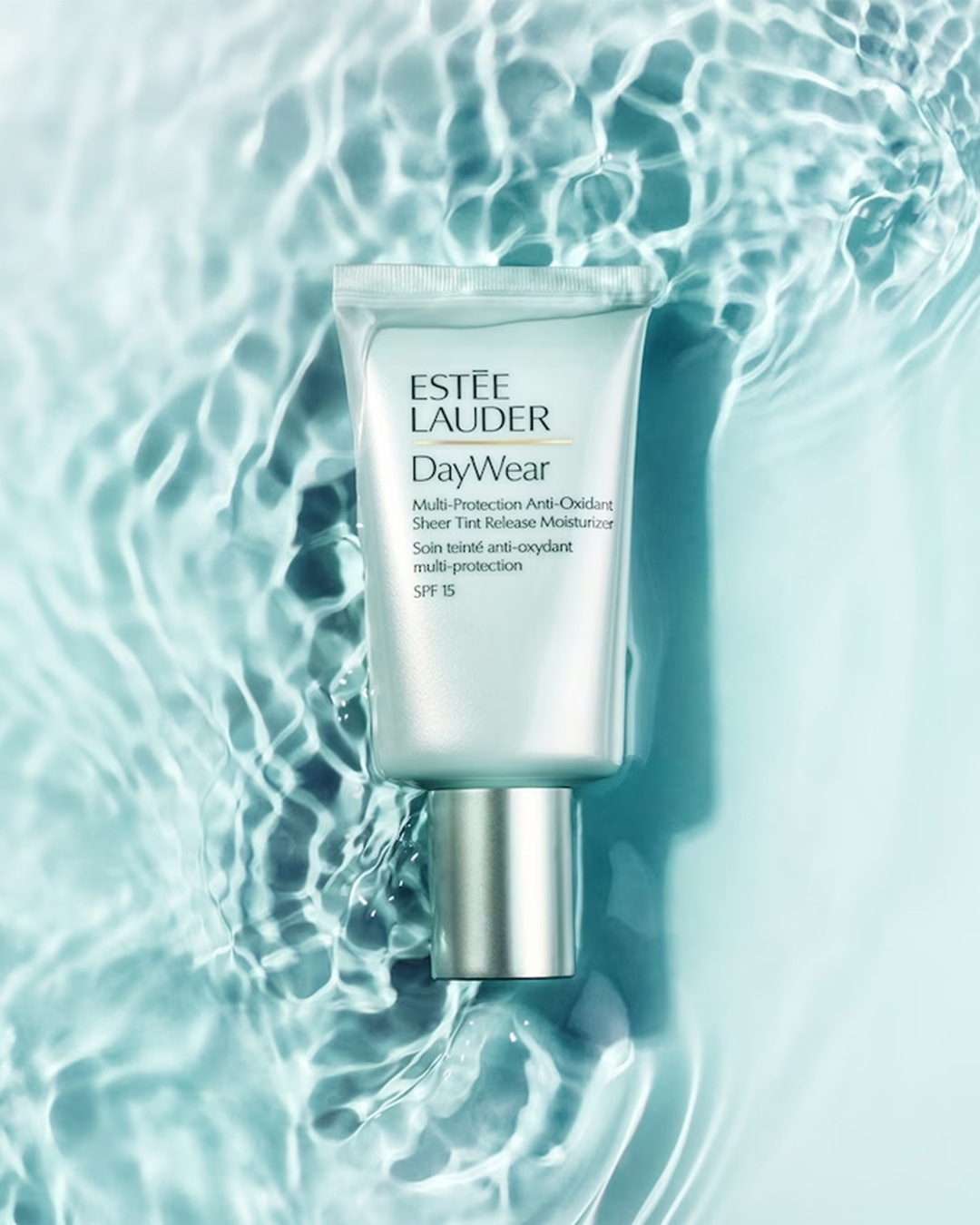 Voici un tube nacré d'Estée Lauder DayWear Multi-Protection Anti-Oxidant Sheer Tint Release Moisturizer SPF 15, flottant sur une eau cristalline.