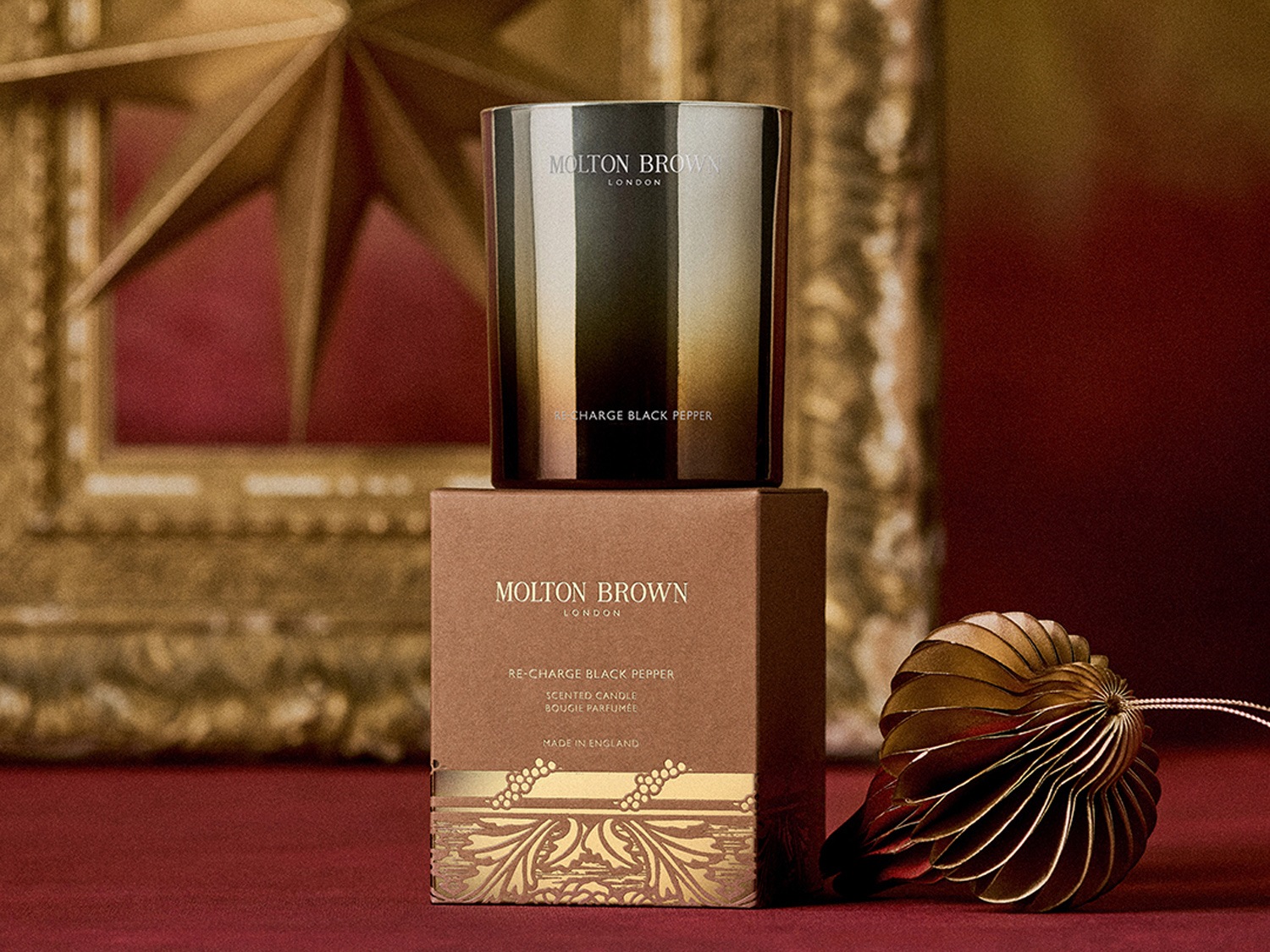 Sviečka Molton Brown London Re-Charge Black Pepper v hnedom balení so zlatými detailmi a ozdobou.