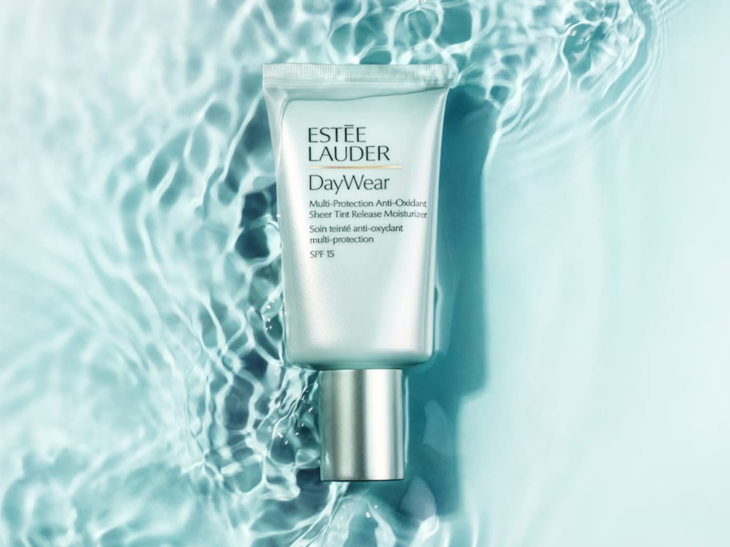 De Estée Lauder DayWear Multi-Protection Anti-Oxidant Sheer Tint Release Moisturizer SPF 15 in een zilveren tube, liggend op een blauwe waterachtergrond.