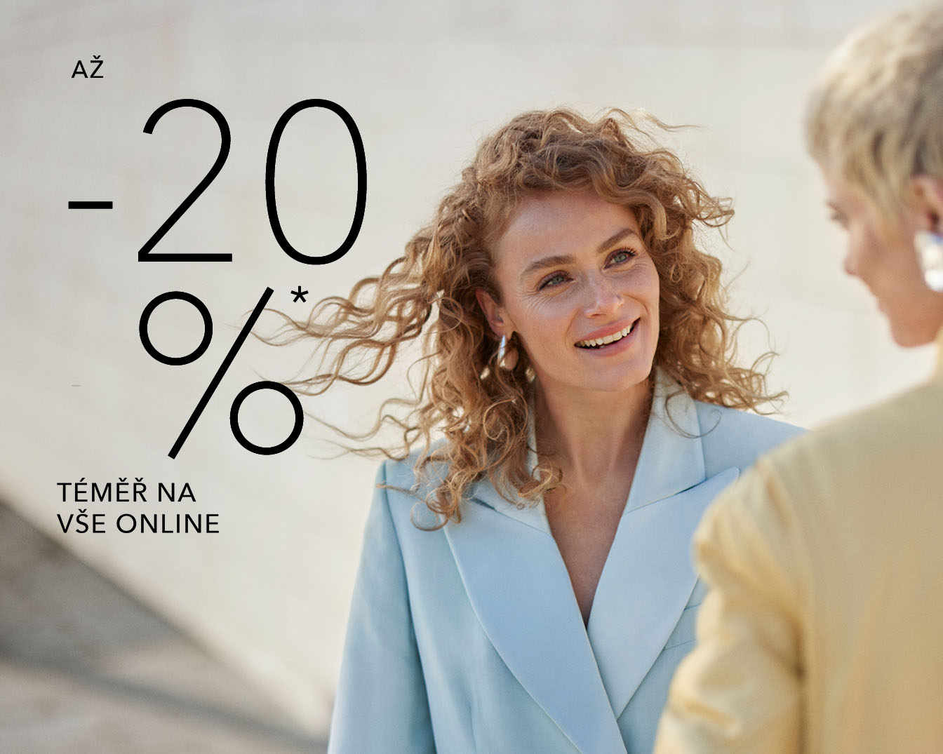 Získejte až 20 % slevu na téměř vše online, žena s kudrnatými vlasy v modrém saku se usmívá.