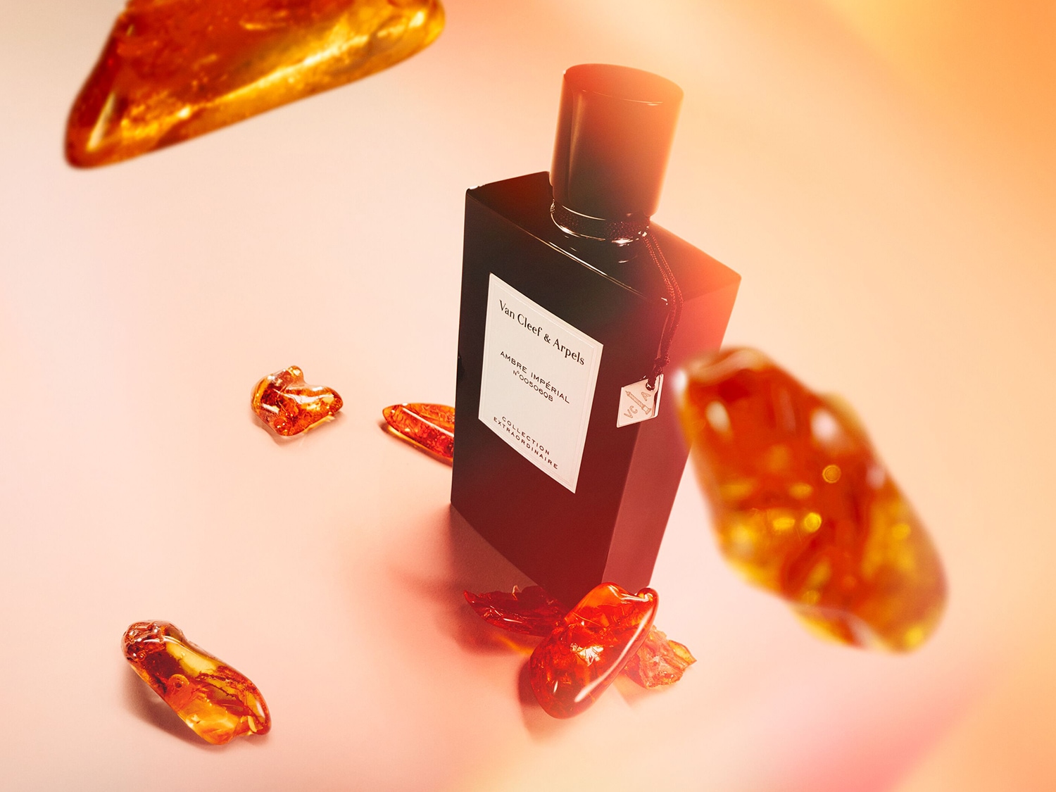 Een zwarte Van Cleef & Arpels Ambre Imperial parfumfles staat tussen stukken amber op een roze achtergrond.
