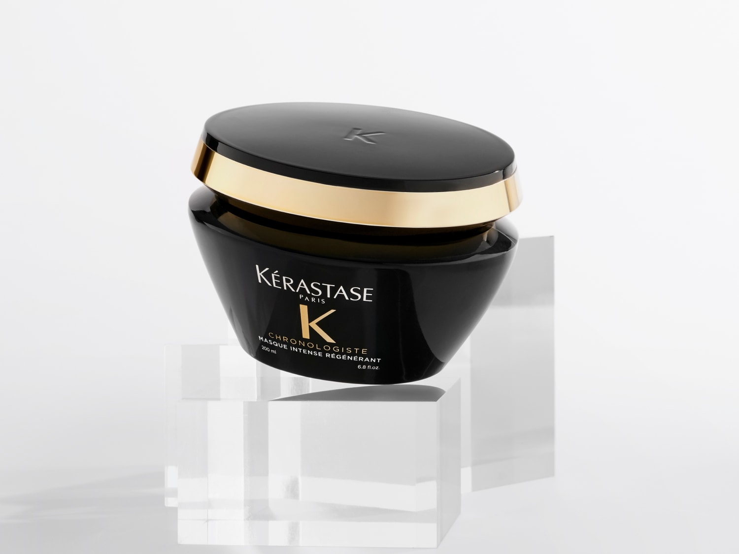 Schwarze Kérastase Chronologiste Maske Intense Régénérant mit goldenem Akzent auf einem transparenten Sockel.