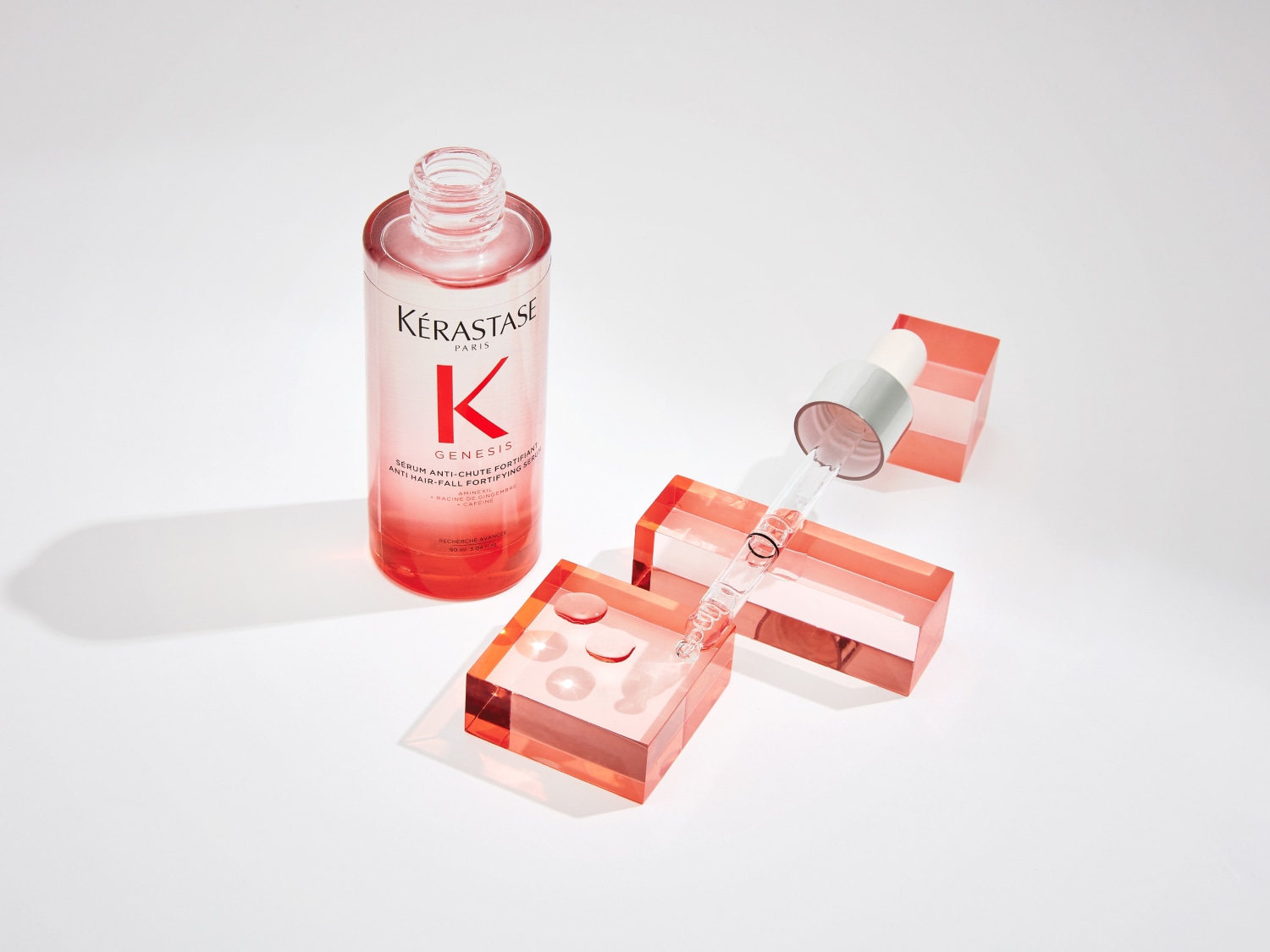 Kérastase Paris Genesis Serum in einer durchsichtigen Flasche mit Pipette, die auf rosa Blöcken liegt, um das Haarwachstum zu fördern.