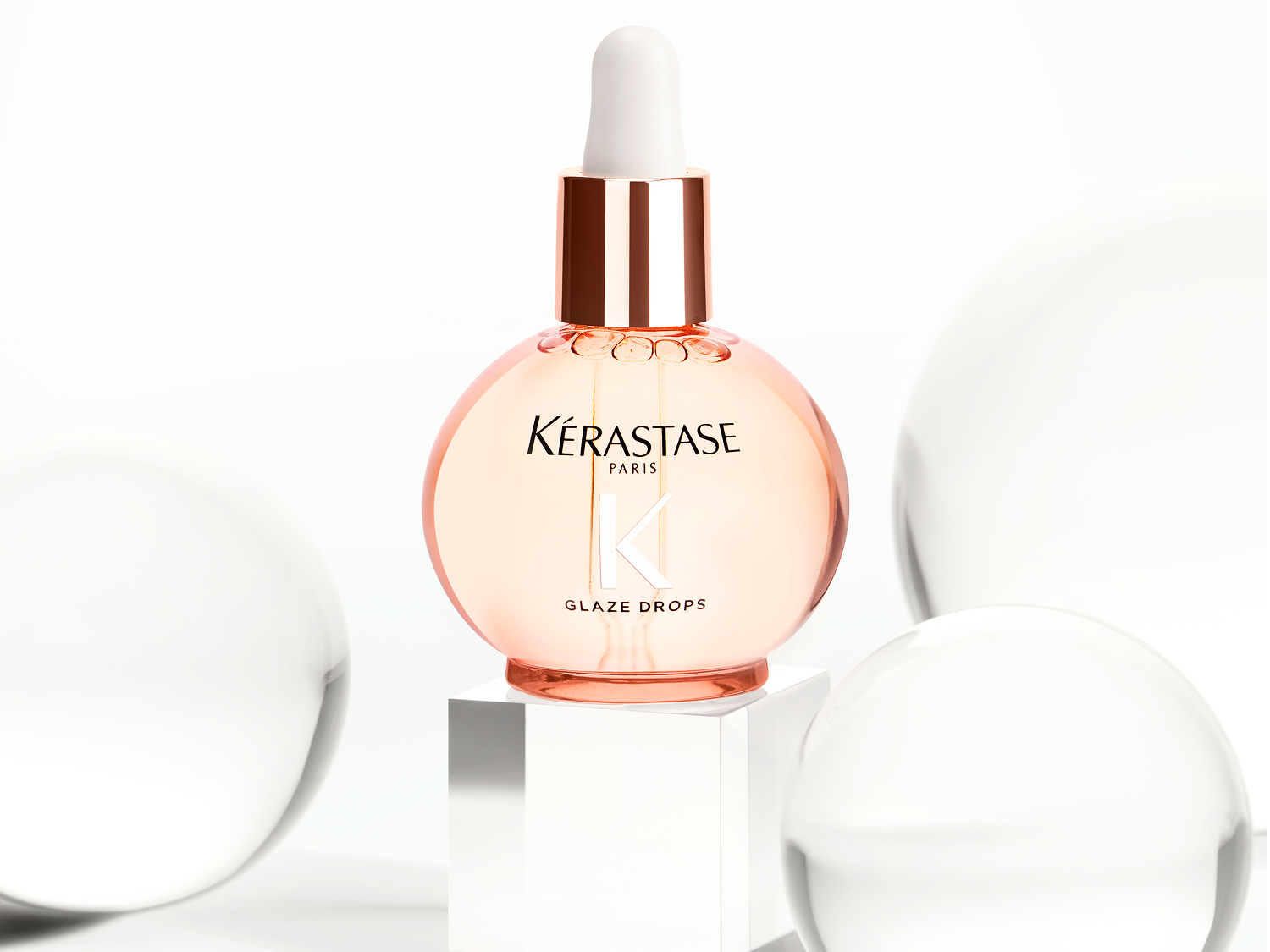 Kérastase Paris Glaze Drops in einer runden, hellrosa Flasche mit Pipette, die auf einem weißen Sockel steht.