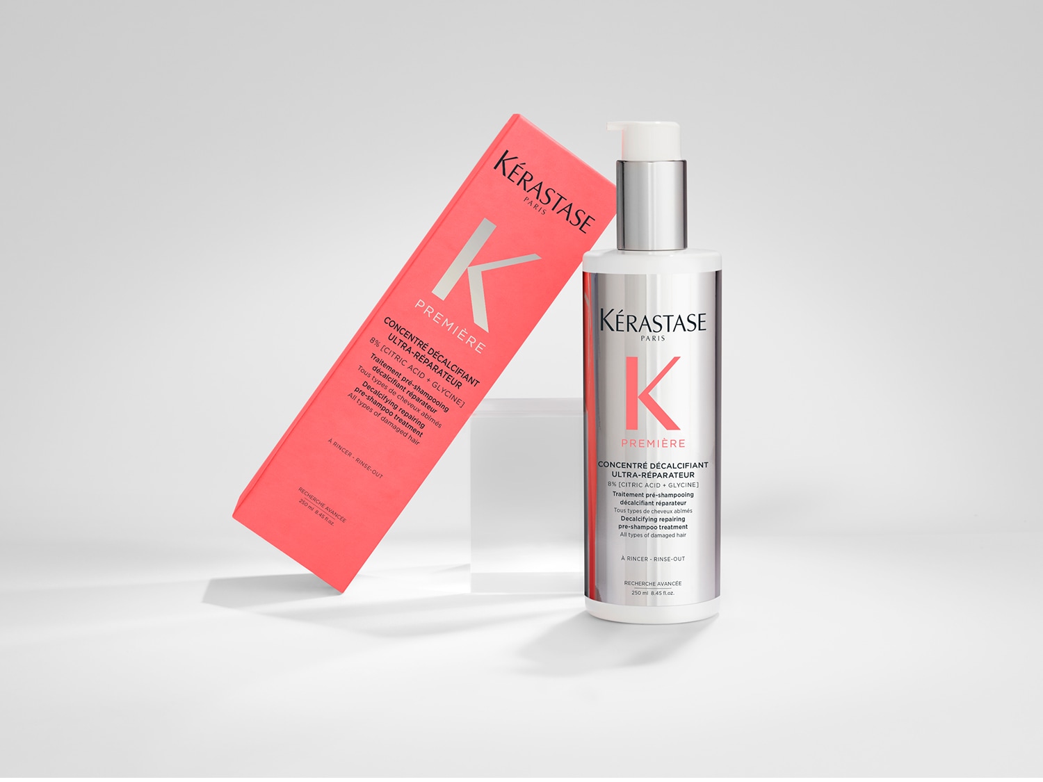 Kérastase Première Concentré Decalcifiant Ultra-Réparateur: Eine Pre-Shampoo-Behandlung mit Zitronensäure und Glycin zur Reparatur von geschädigtem Haar, präsentiert in einer silbernen Flasche mit Pumpe und einer korallfarbenen Verpackung.