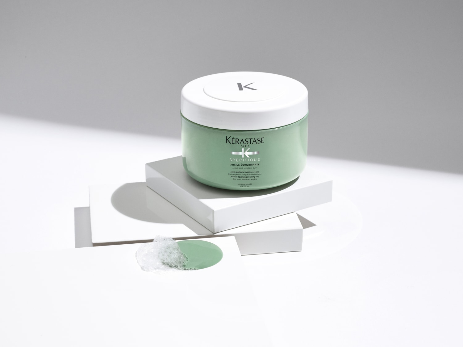 Die grüne Dose Kérastase Spécifique Argile Équilibrante auf weißen Blöcken verspricht eine reinigende Tonerde für fettige Wurzeln und sensible Längen.