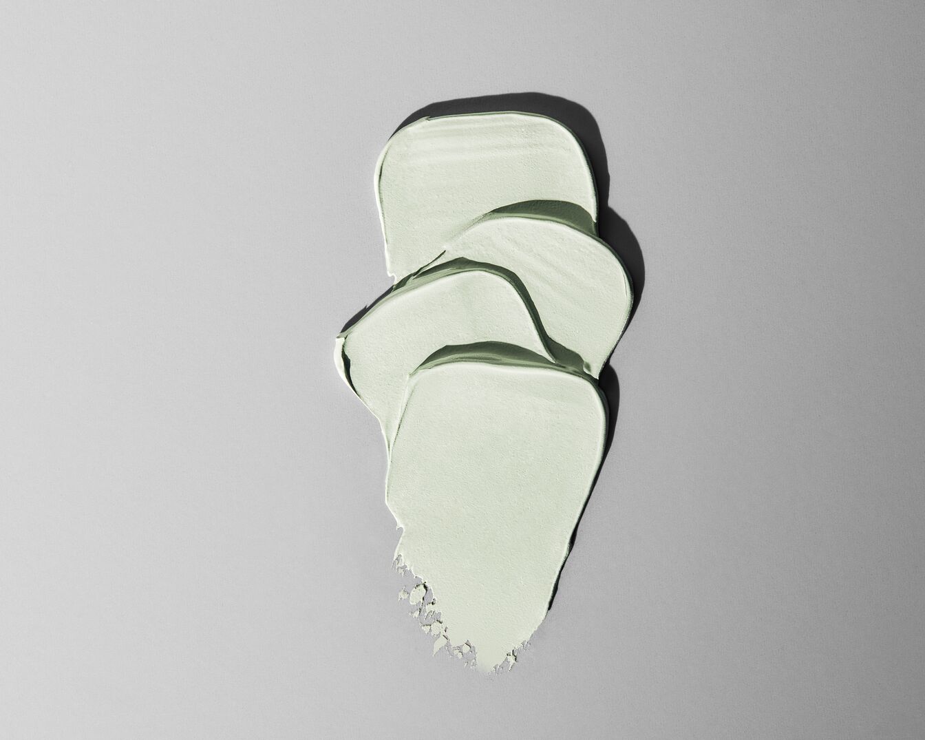 Textuur van een lichtgroen cosmetisch product, zoals een masker of crème, uitgesmeerd op een grijze achtergrond.