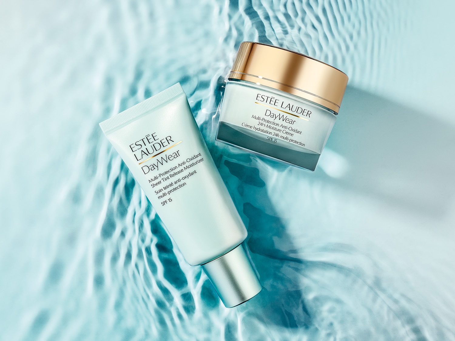 Auf blauem Wasser liegen eine Tube und ein Tiegel der Estée Lauder DayWear-Serie, die mit Antioxidantien schützt und Feuchtigkeit spendet, beide mit LSF 15.