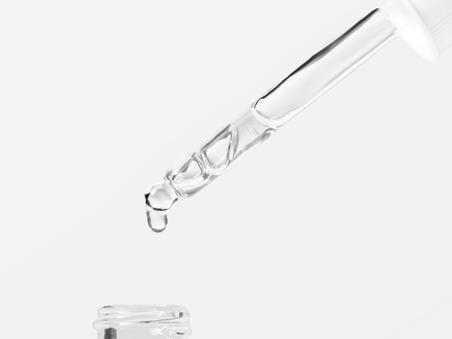 Close-up van een helder serum dat uit een glazen pipet druppelt, klaar om de huid te hydrateren en te laten stralen.