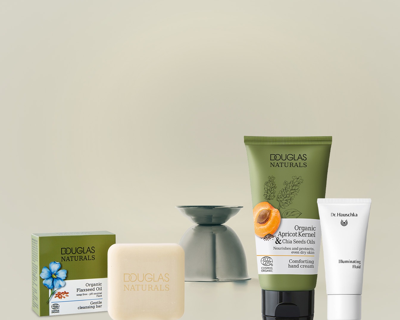 Una selezione di prodotti di bellezza naturali, tra cui un sapone detergente delicato all'olio di lino, una crema mani confortante con olio di nocciolo di albicocca e semi di chia, e un fluido illuminante.