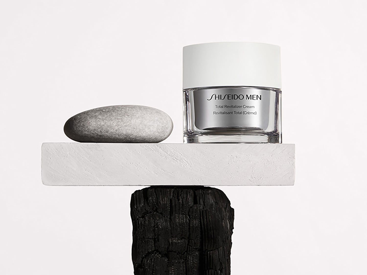 Crema revitalizante total Shiseido Men en envase de vidrio transparente con tapa blanca, sobre una base de piedra y madera.