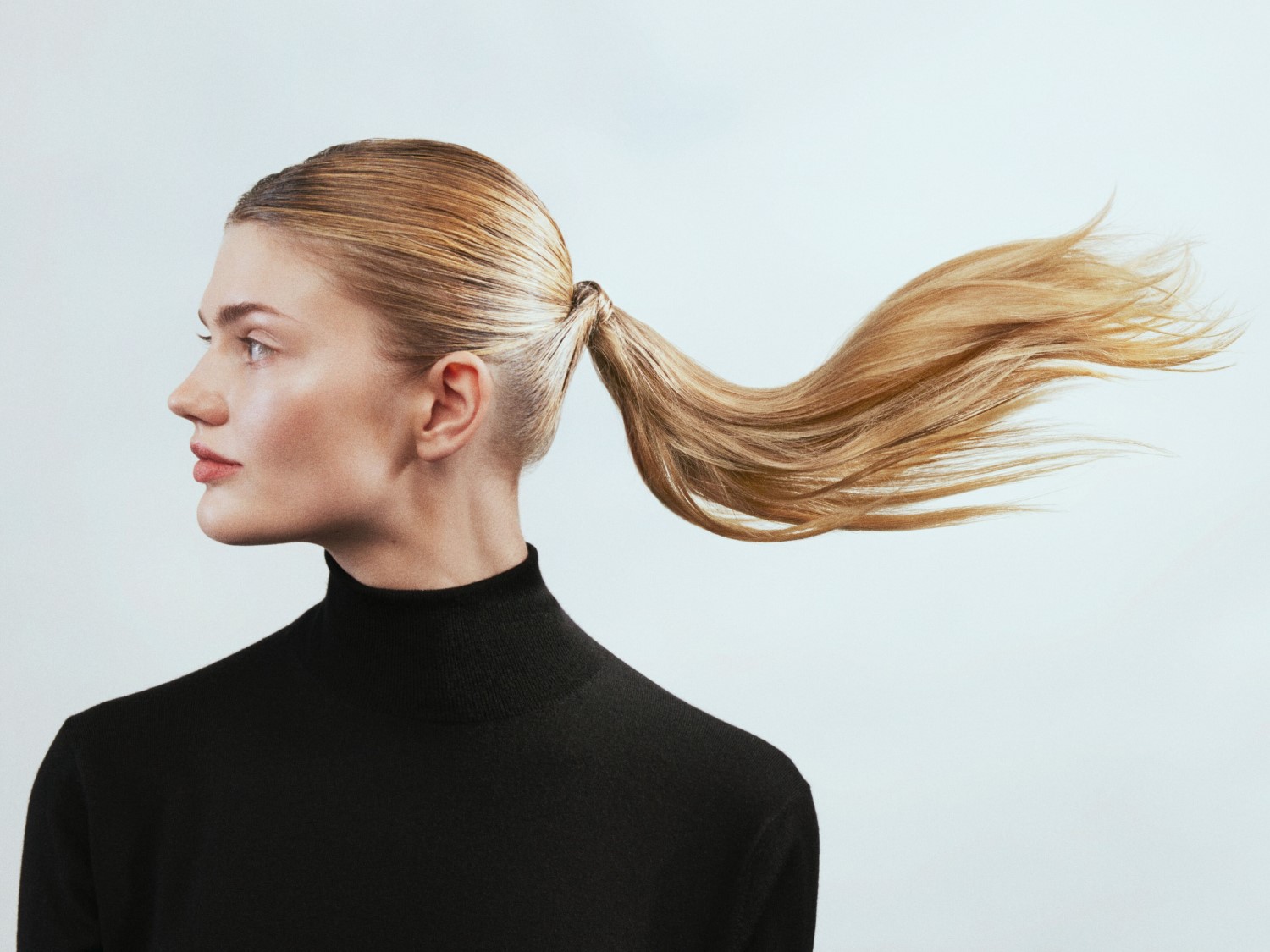 Profiel van een blonde vrouw met een zwarte coltrui en een paardenstaart die naar rechts waait.
