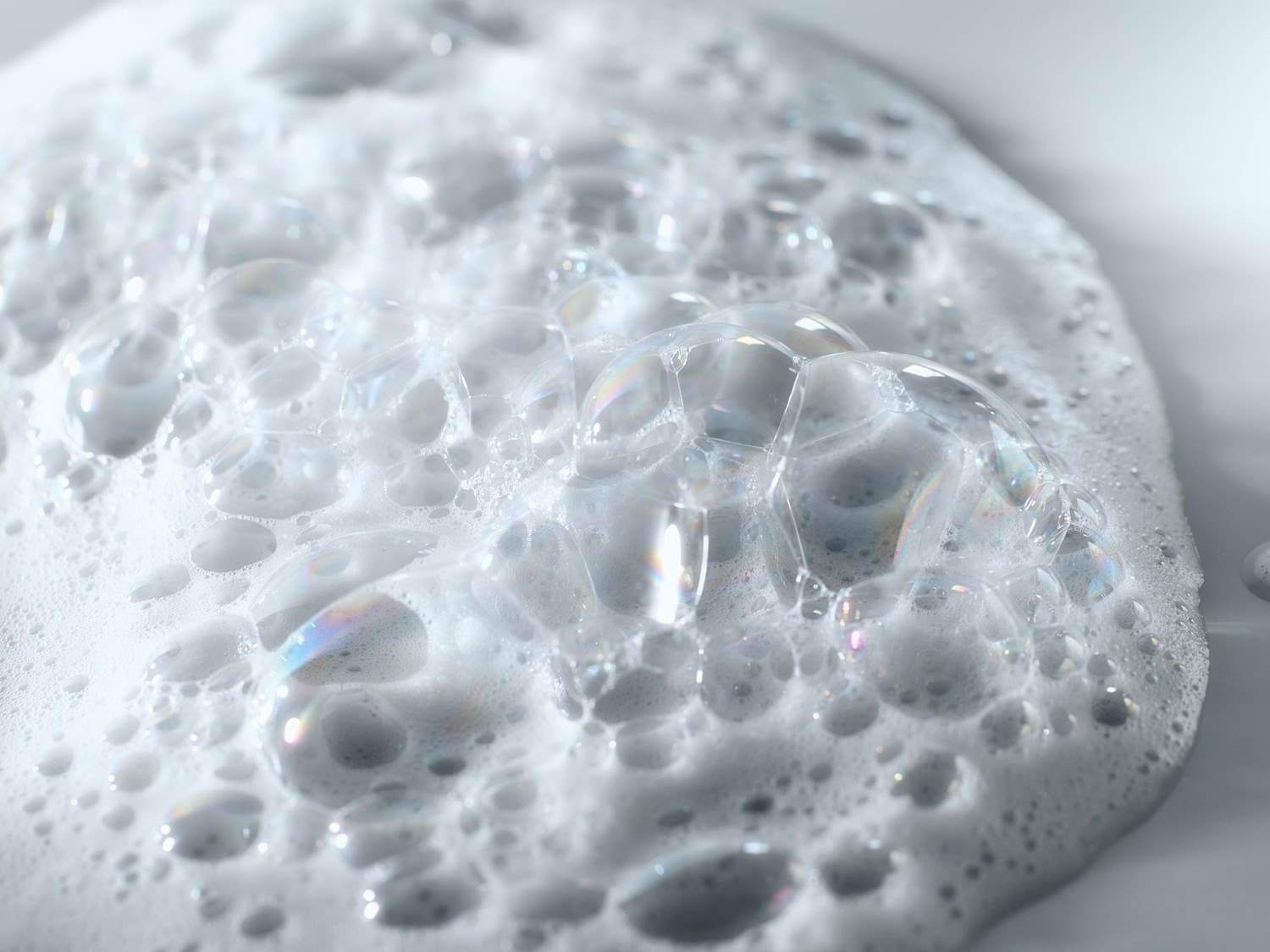 Nahaufnahme von schäumender, weißer Seife mit irisierenden Blasen, die eine reinigende und erfrischende Textur suggerieren.