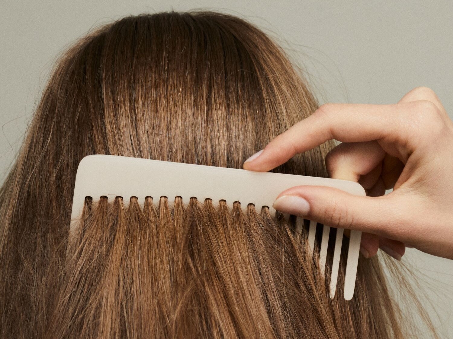 Nahaufnahme von einer Person, die ihre langen, braunen Haare mit einem hellen Kamm kämmt.