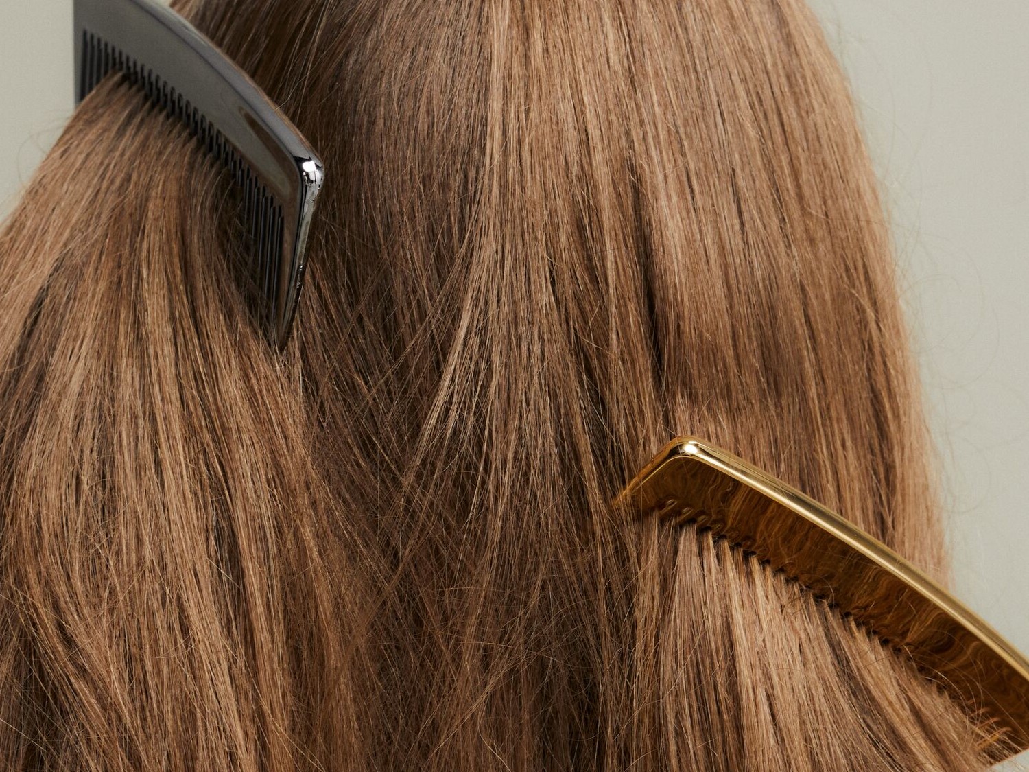 Nahaufnahme von hellbraunem, glattem Haar, das mit einem schwarzen und einem goldenen Kamm gestylt wird.