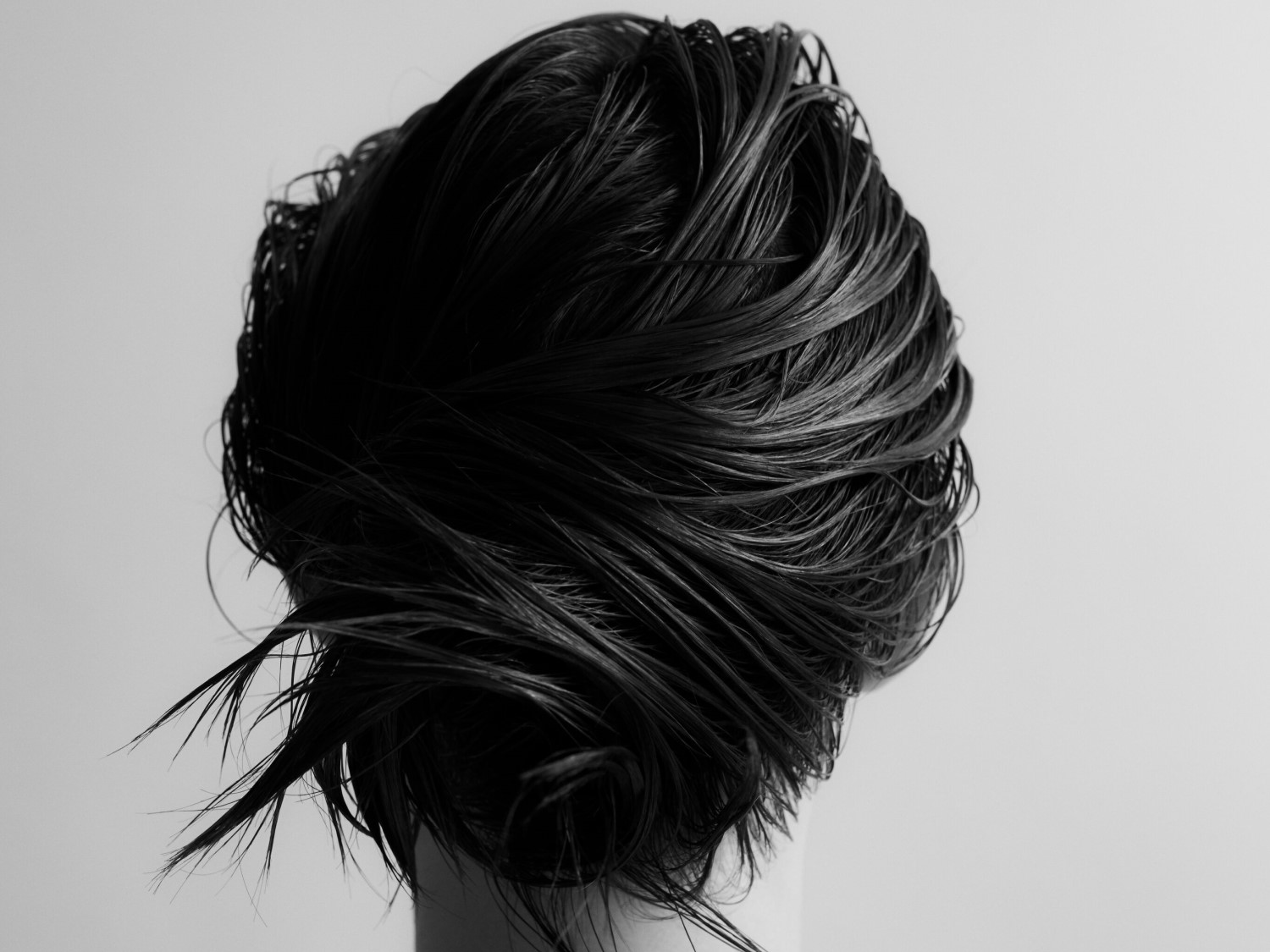 Nahaufnahme von dunklem, nassem Haar, das zu einem Knoten geformt wurde und einen glänzenden, gepflegten Look erzeugt.