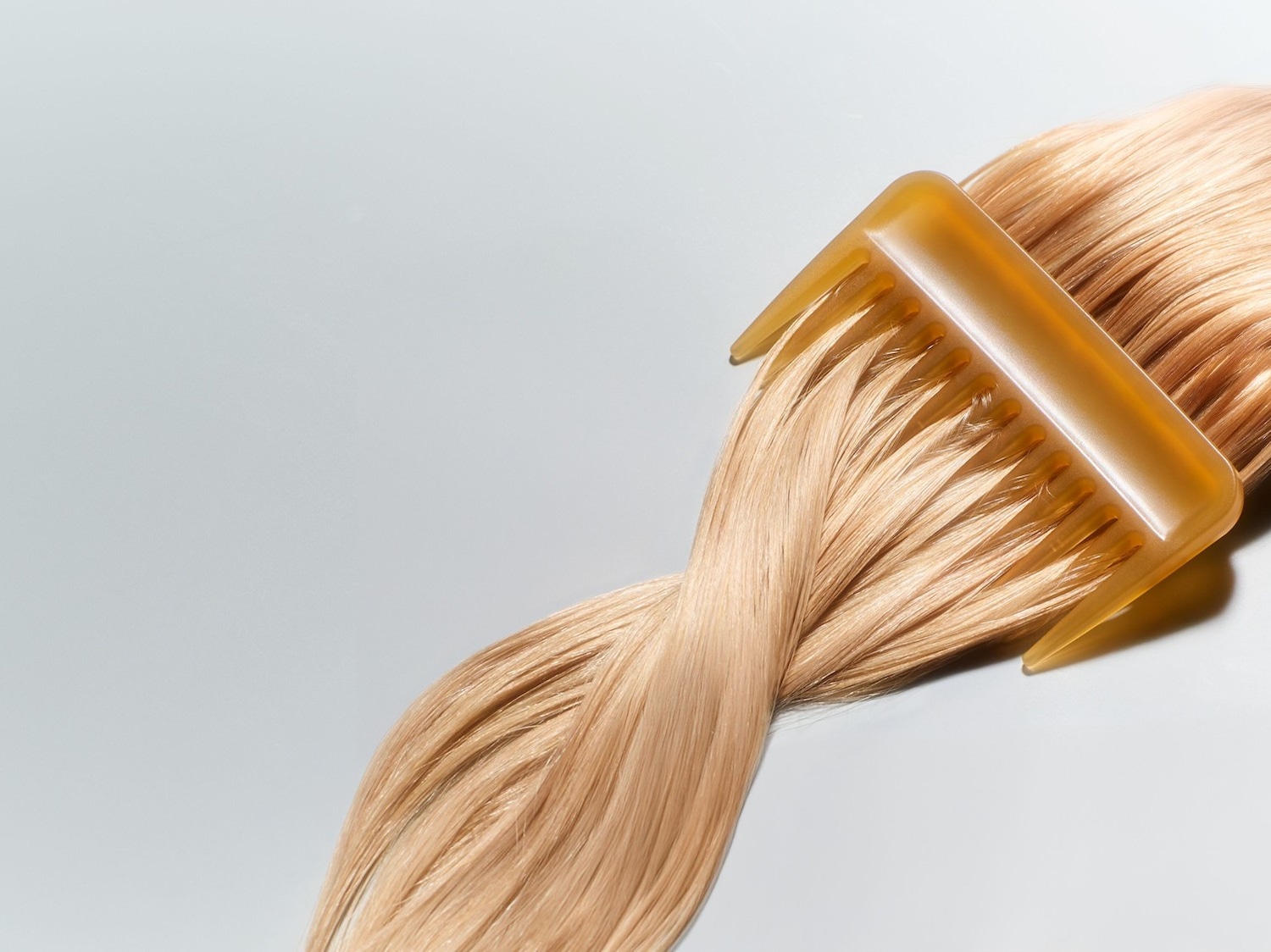 Nahaufnahme von blondem, gewelltem Haar, das mit einem bernsteinfarbenen Kamm gekämmt wird, um die Haarpflege und das Styling hervorzuheben.