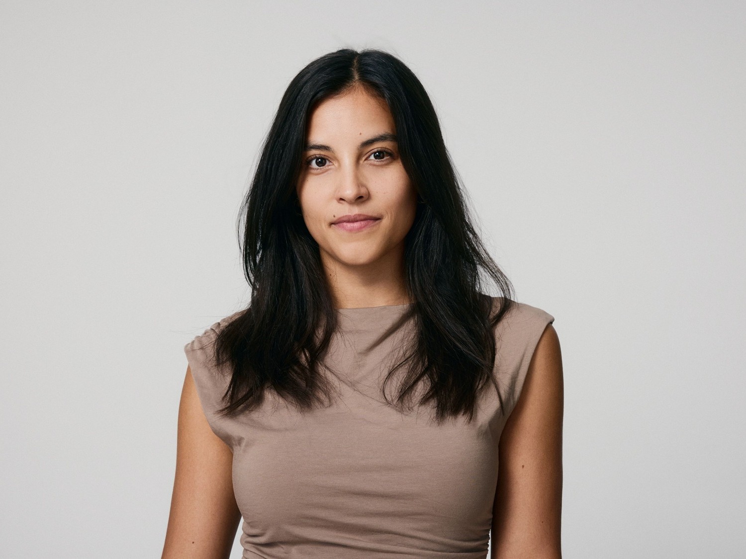 Eine Frau mit langen, dunklen Haaren und einem hellbraunen Oberteil blickt direkt in die Kamera.