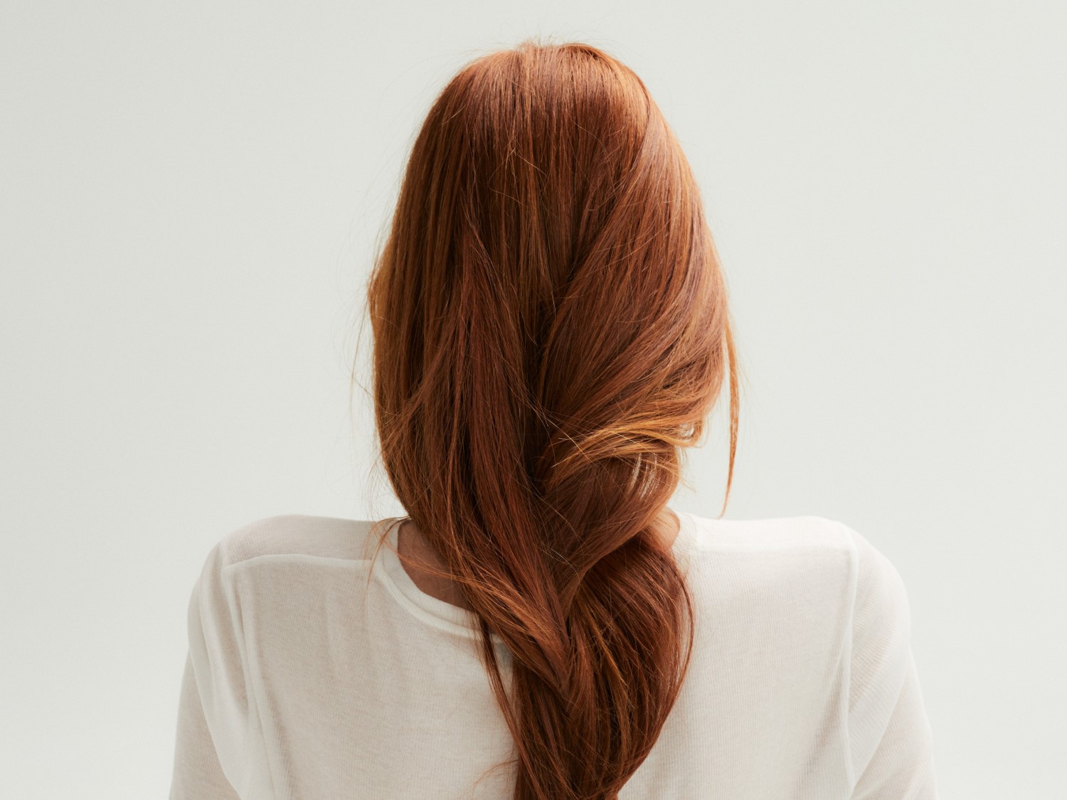 Eine Frau mit langen, gewellten, roten Haaren, die zu einem lockeren Zopf geflochten sind, trägt ein weißes Oberteil.