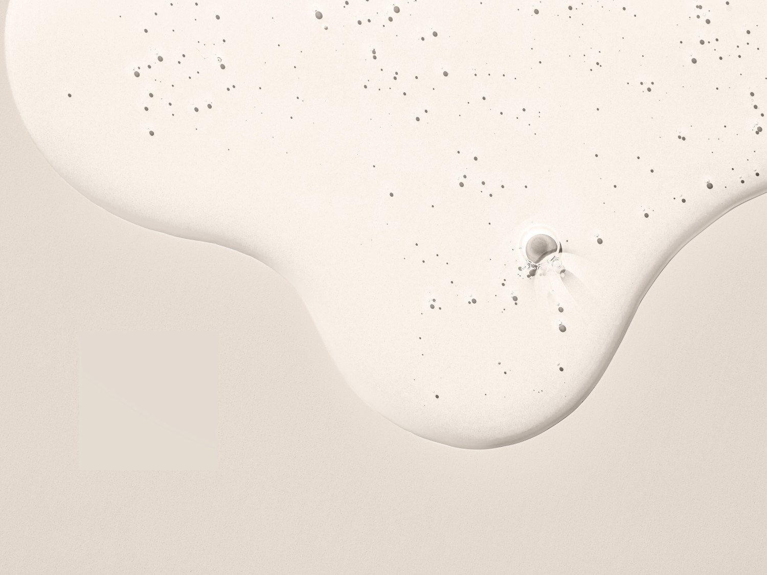 Nahaufnahme einer transparenten, leicht getönten Flüssigkeit mit kleinen Bläschen, die eine glatte, reflektierende Oberfläche bildet.