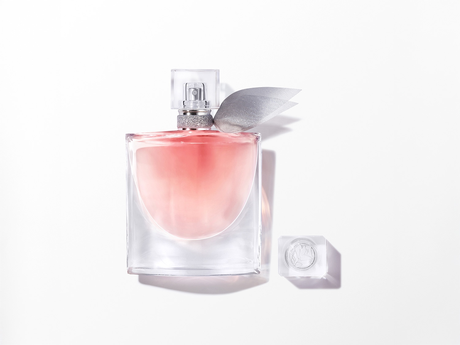 Ein elegantes Parfüm präsentiert sich in einem klaren Glasflakon mit einem zarten rosa Farbton, verziert mit einer silbernen Schleife und einem transparenten Verschluss.