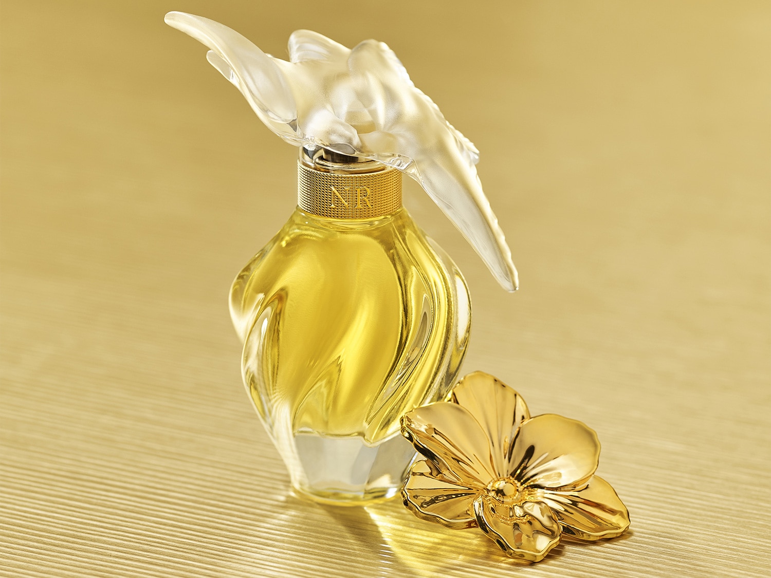 Découvrez le parfum Nina Ricci dans son flacon doré, orné d'une fleur dorée et d'un bouchon en forme d'oiseau transparent, une essence de luxe et de féminité.