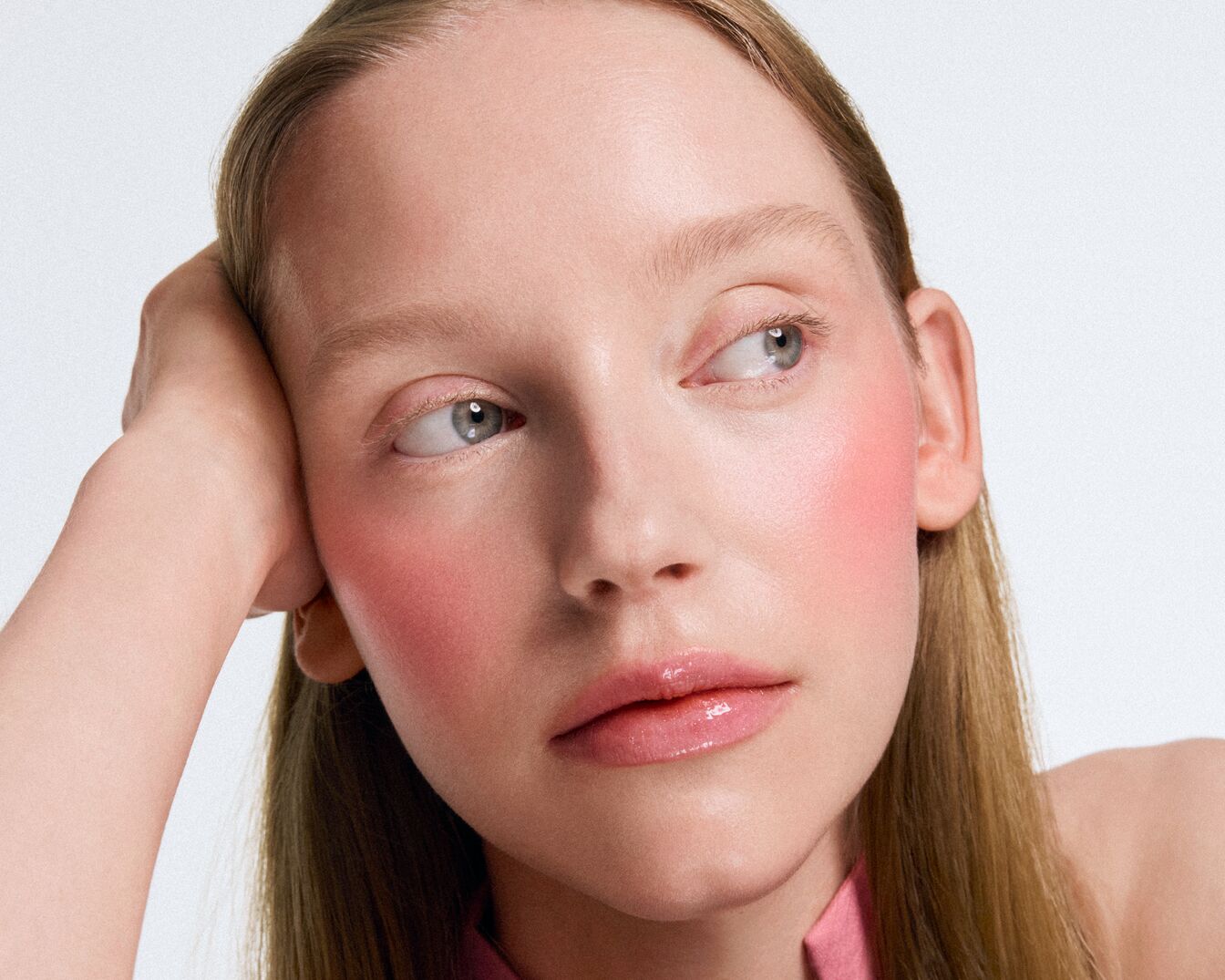 Nahaufnahme eines hellhäutigen Models mit rosa Rouge und glänzenden Lippen, das zur Seite schaut.