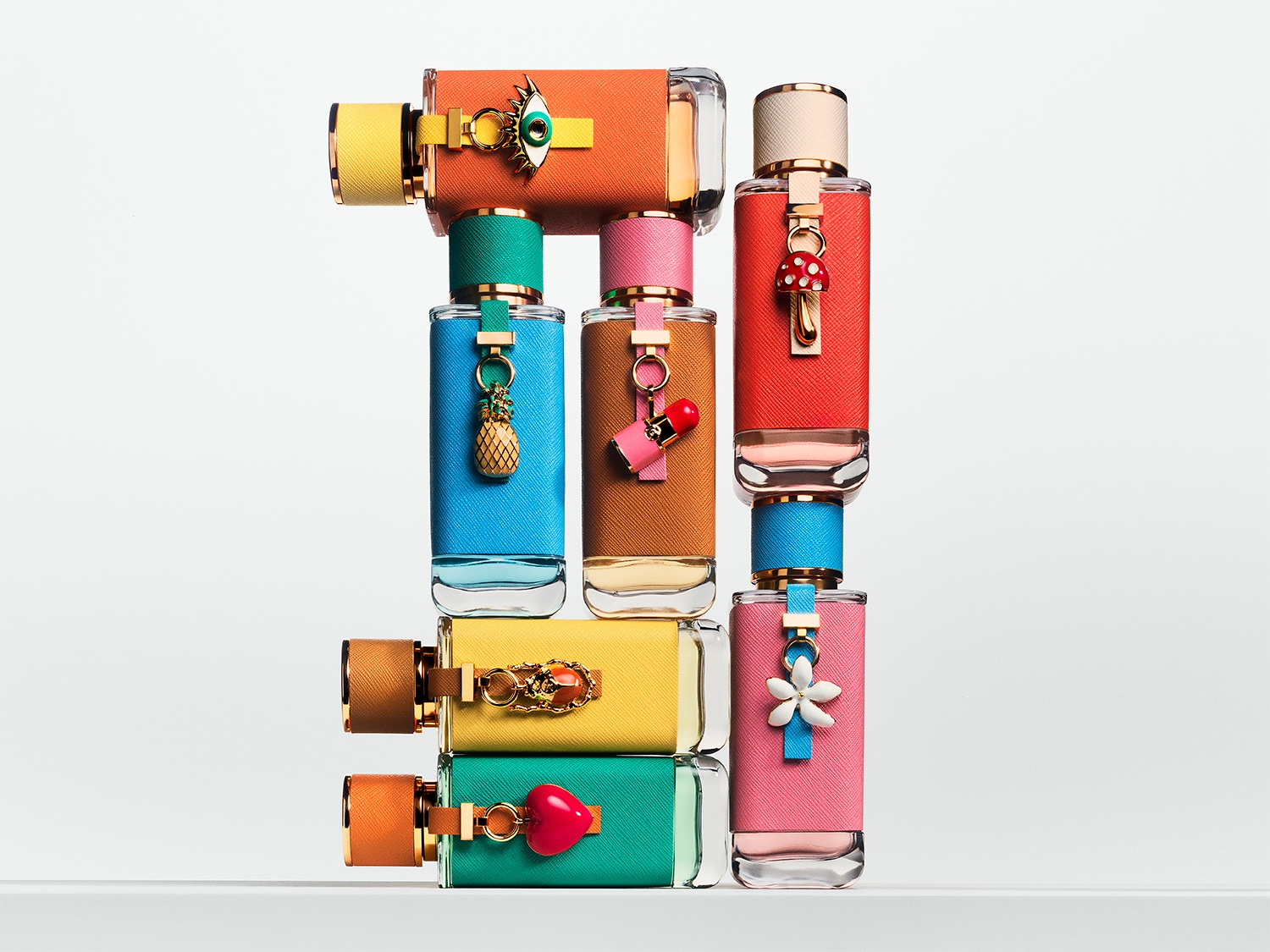 Eine gestapelte Sammlung von Prada-Parfümflaschen in verschiedenen Farben, jede mit einem einzigartigen Anhänger, der dem Duft eine verspielte Note verleiht.