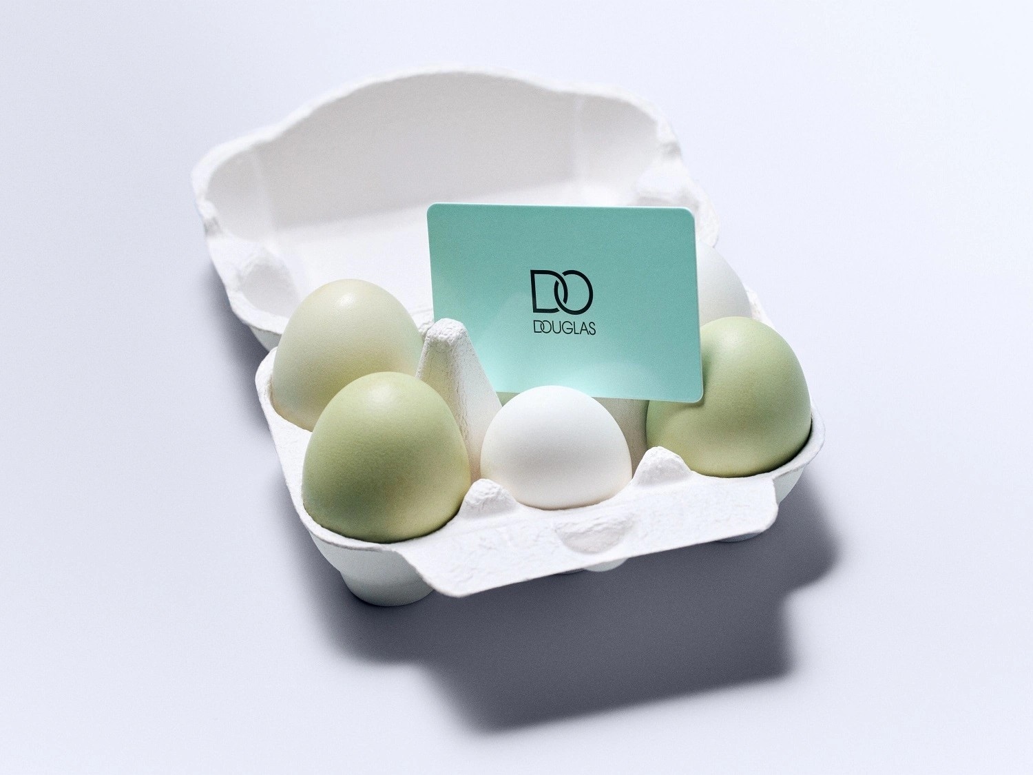 Eierschachtel mit grün und weiss gefärbten Eiern und einer hellblauen Douglas Geschenkkarte.