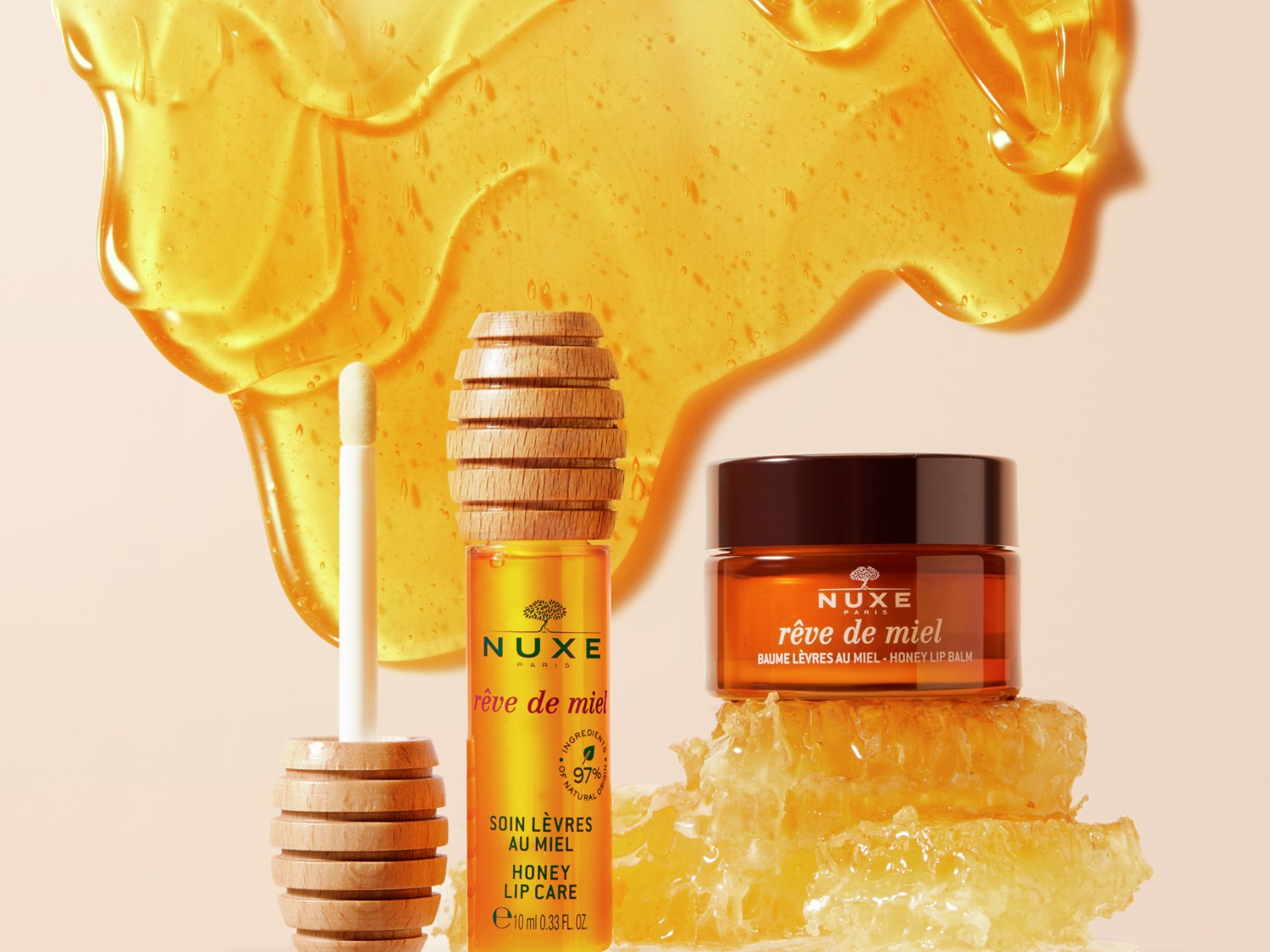 Nuxe Rêve de Miel lippenverzorgingsproducten, waaronder een honinglippenbalsem in een bruine pot en een honinglippenverzorging in een heldere tube met een houten applicator, tegen een achtergrond van honing.