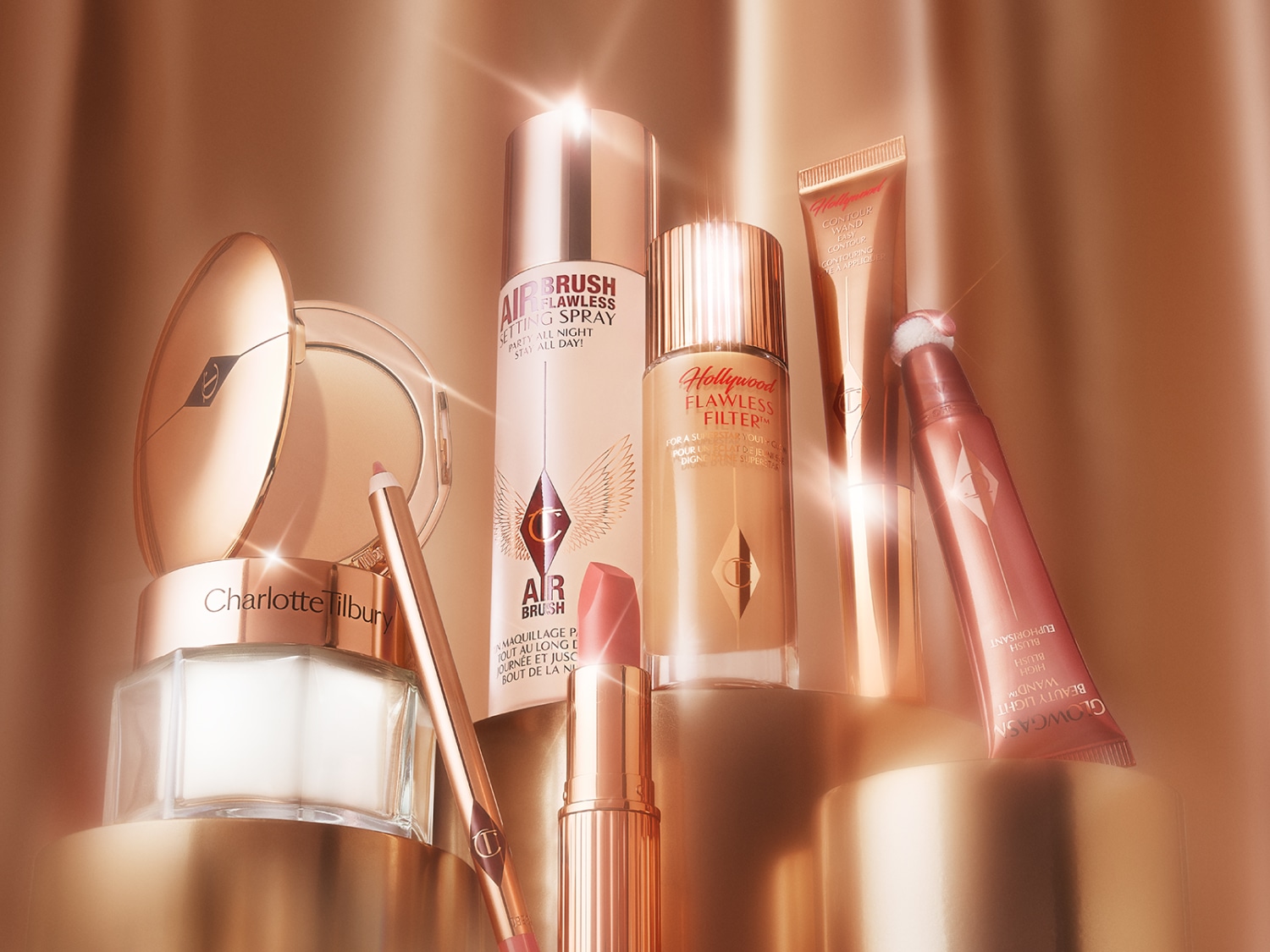 Eine Sammlung von Charlotte Tilbury Make-up Produkten in Goldtönen, darunter Puder, Spray, Filter, Lippenstift und Rouge.