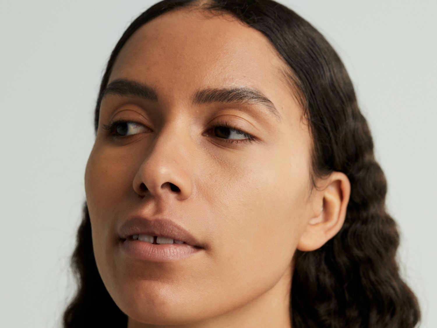 Nahaufnahme eines Frauengesichts mit glatter, ebenmäßiger Haut, dunklen, gewellten Haaren und einem sanften, natürlichen Make-up, das ihre Gesichtszüge betont.