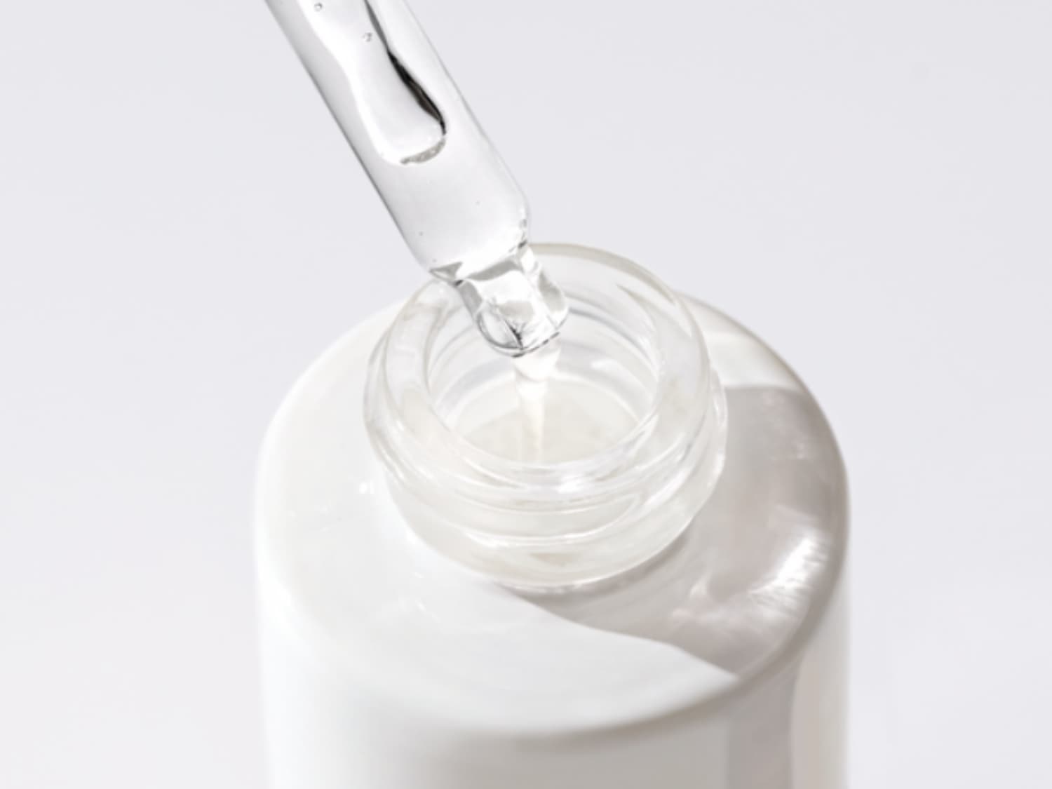 Un flacone bianco aperto con un contagocce trasparente che rilascia un siero chiaro, ideale per la cura della pelle.