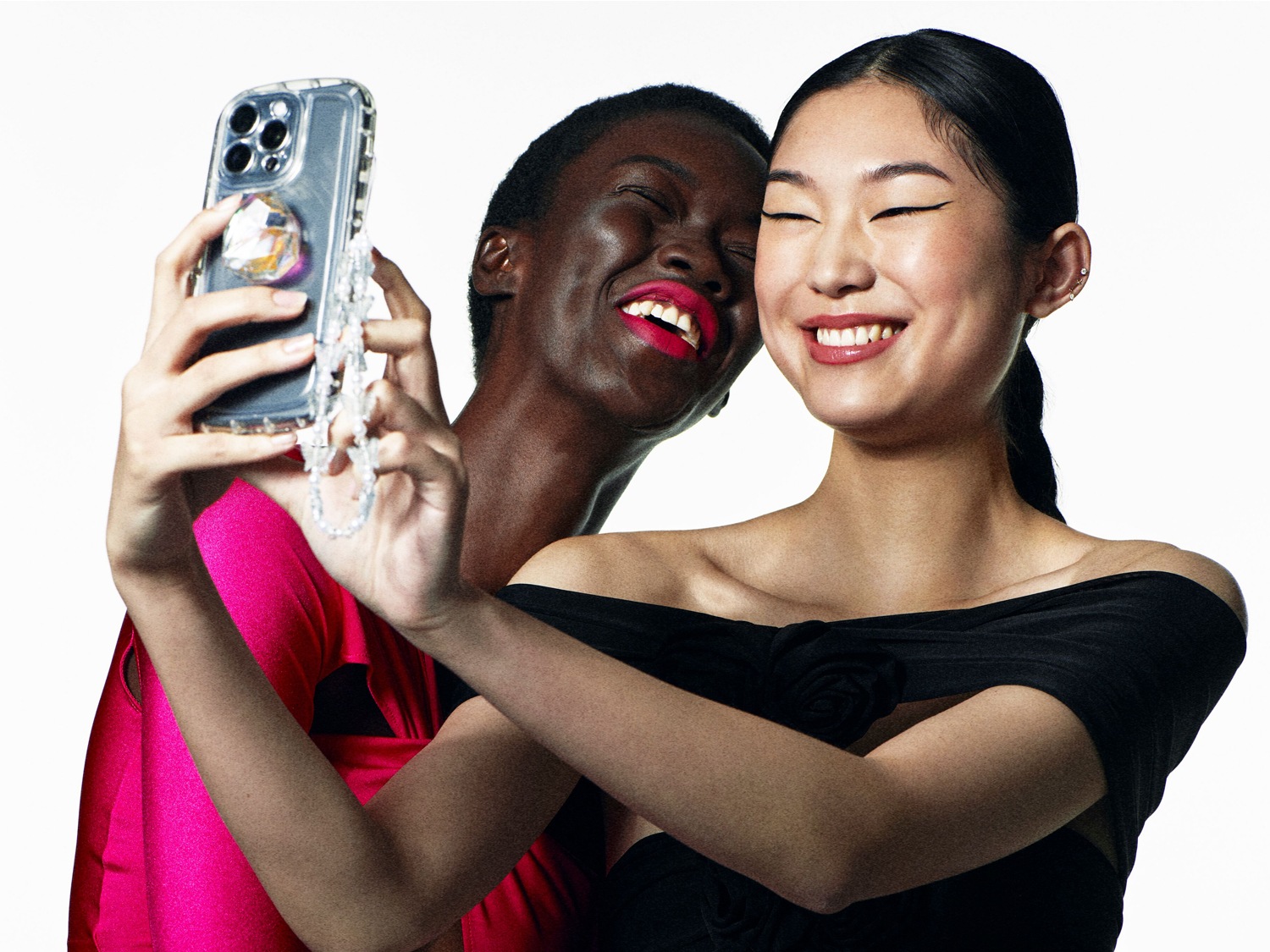 Twee lachende vrouwen maken een selfie met een telefoon met een doorzichtig hoesje en een strass hanger.