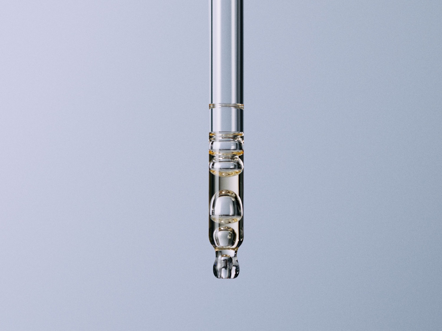 Primer plano de un gotero de vidrio transparente lleno de un suero dorado, mostrando su textura y consistencia.