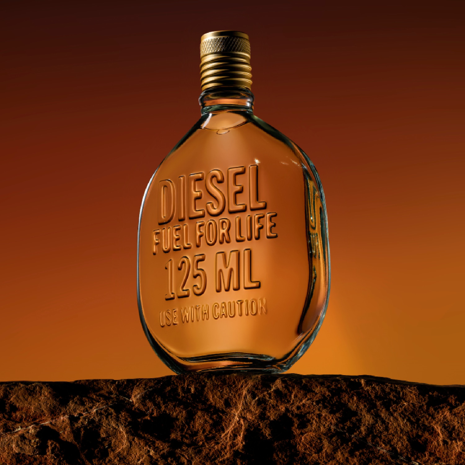 Un flacon de parfum ambré Diesel Fuel for Life de 125 ml, au design ovale et embossé, est posé sur une roche sombre. Le flacon est surmonté d’un bouchon doré à motif strié, et l’ensemble est mis en valeur par un fond dégradé orange évoquant un coucher de soleil désertique.