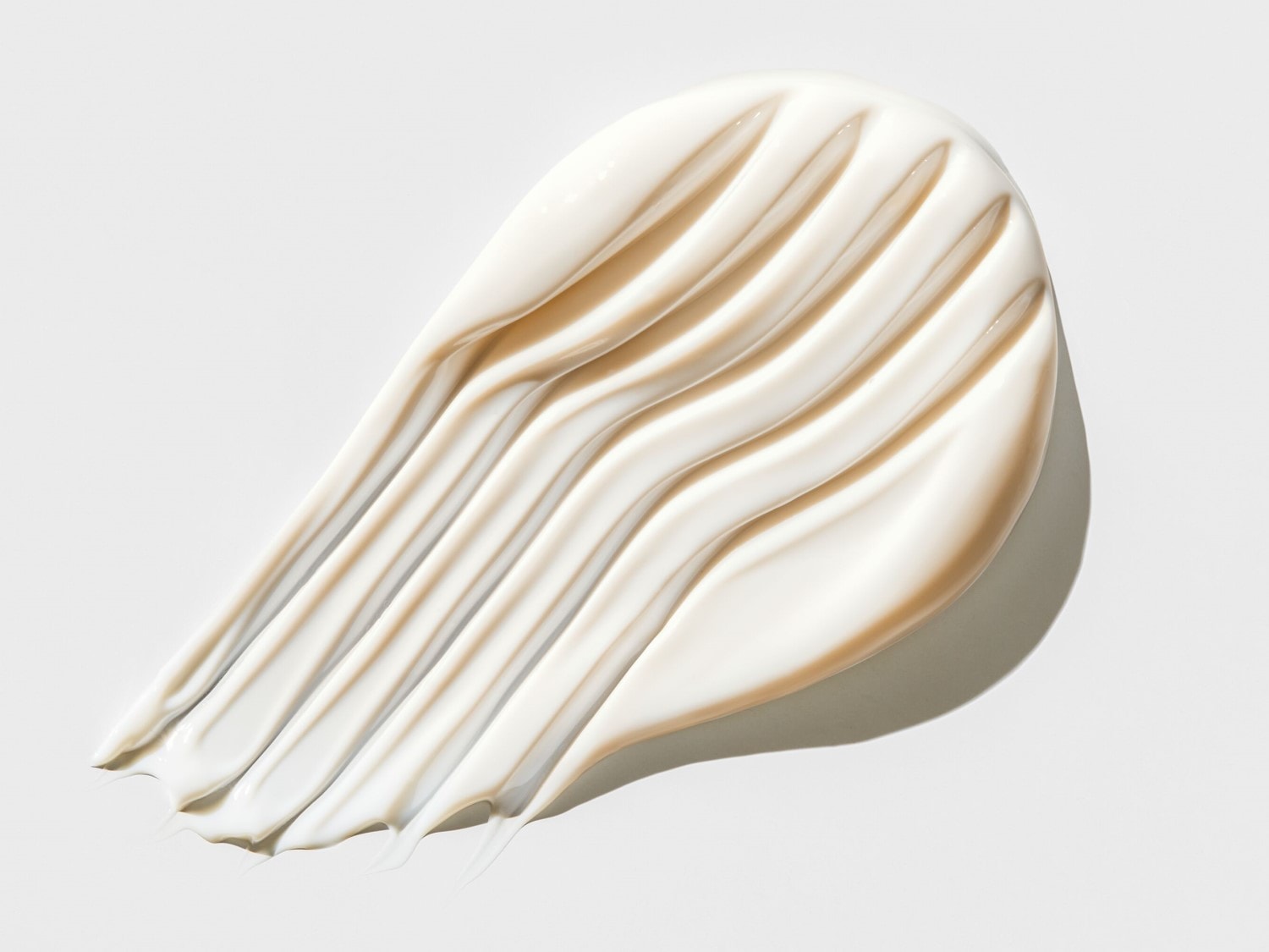 Švelnus kreminės tekstūros tepinėlis ant balto paviršiaus, demonstruojantis produkto tirštumą ir švelnumą.