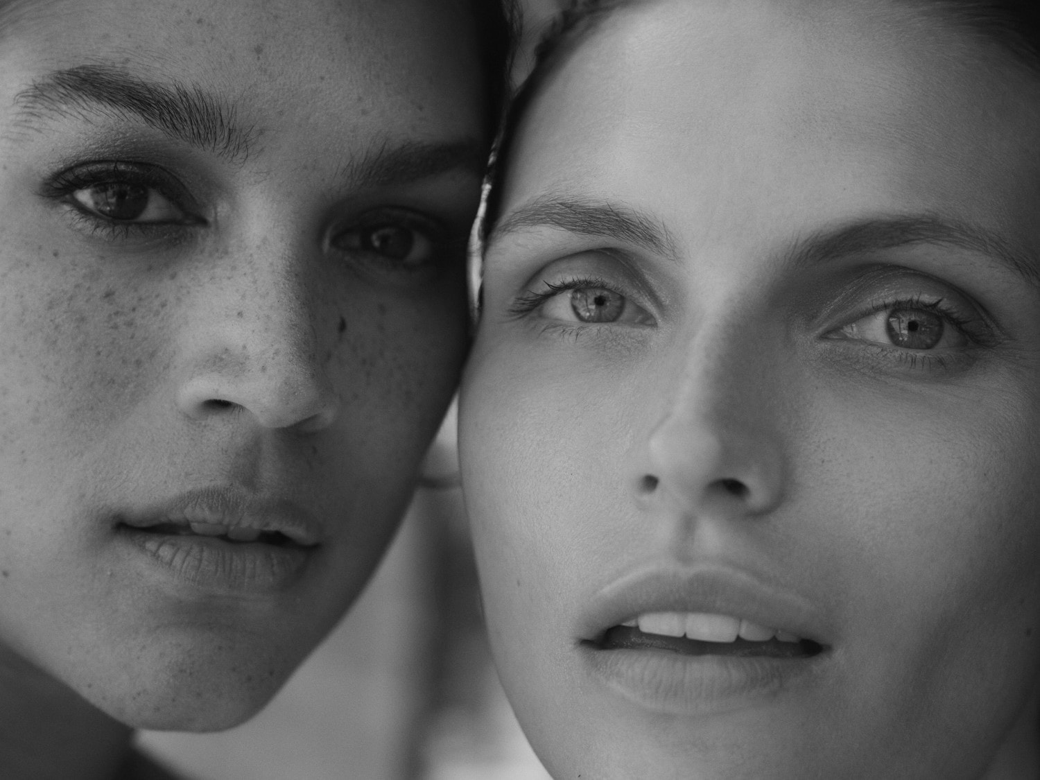 Juodai balta nuotrauka, kurioje matomi dviejų moterų veidai, vienos su strazdanomis, o kitos su šviesia oda, žiūrinčios tiesiai į priekį.