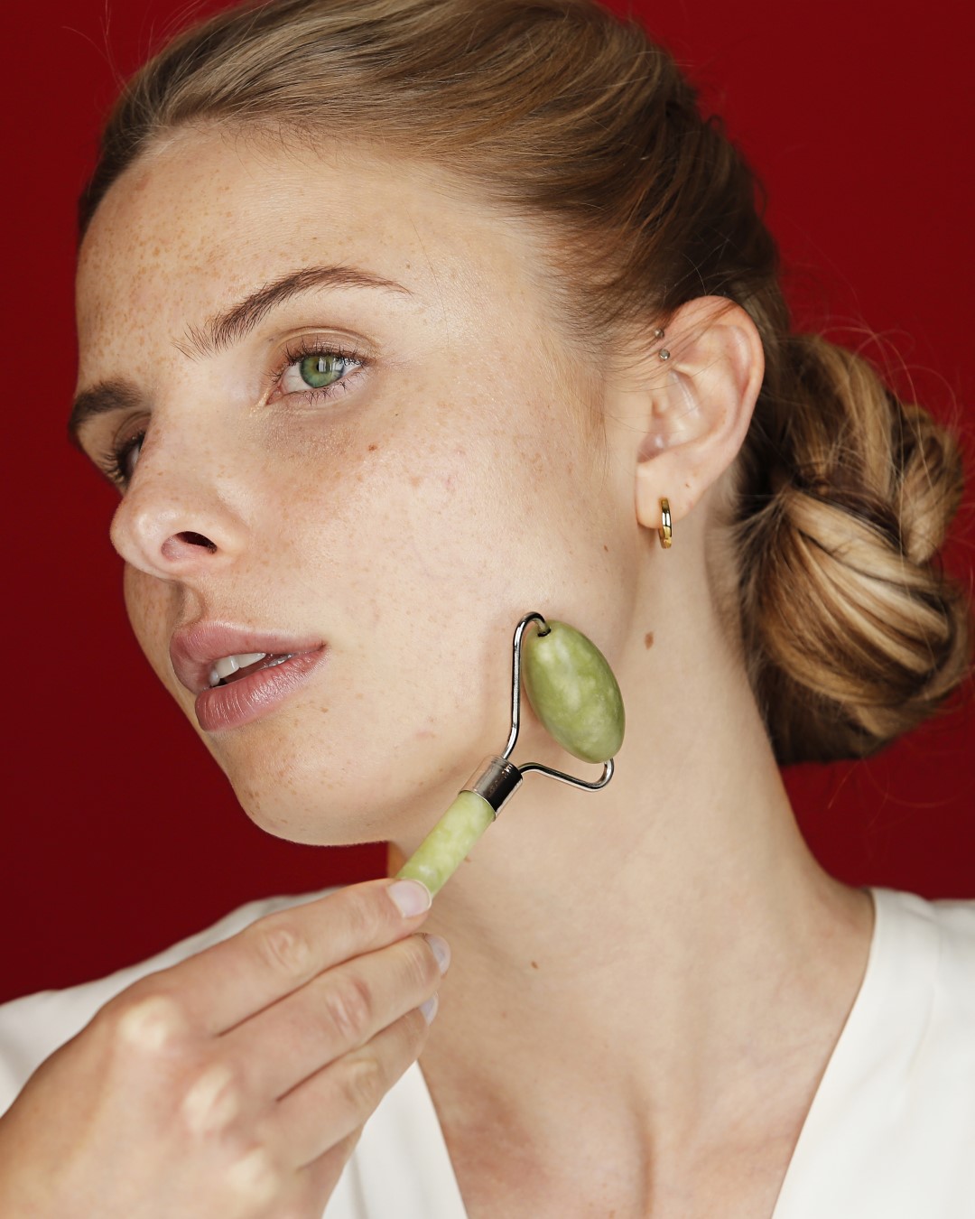 Eine Frau mit blonden Haaren und Sommersprossen benutzt einen Jadewalze auf ihrer Wange, um die Durchblutung zu fördern und die Haut zu straffen.