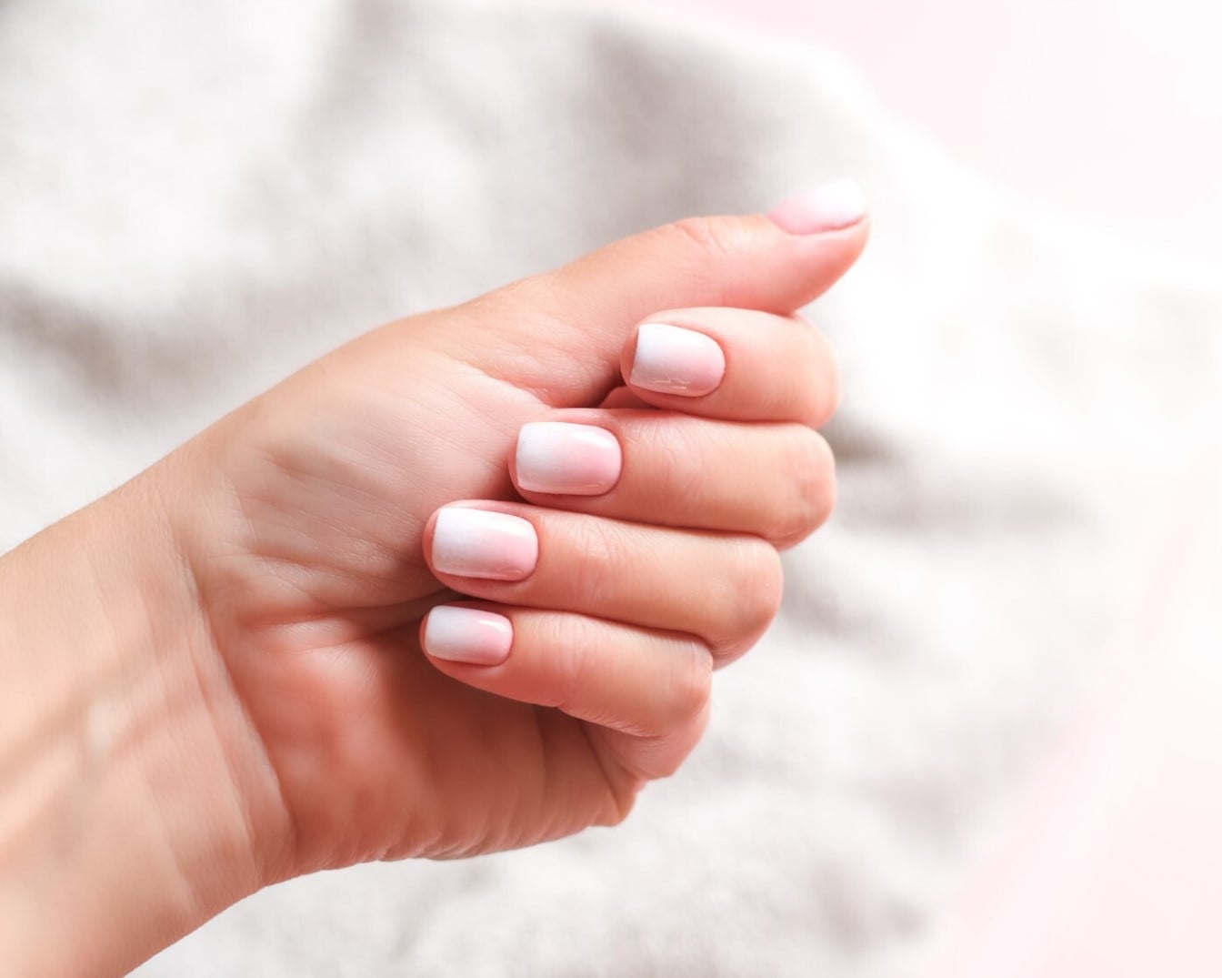 Nahaufnahme einer Hand mit Ombre-Nägeln, die von zartrosa zu weiß übergehen und einen eleganten und gepflegten Look zeigen.