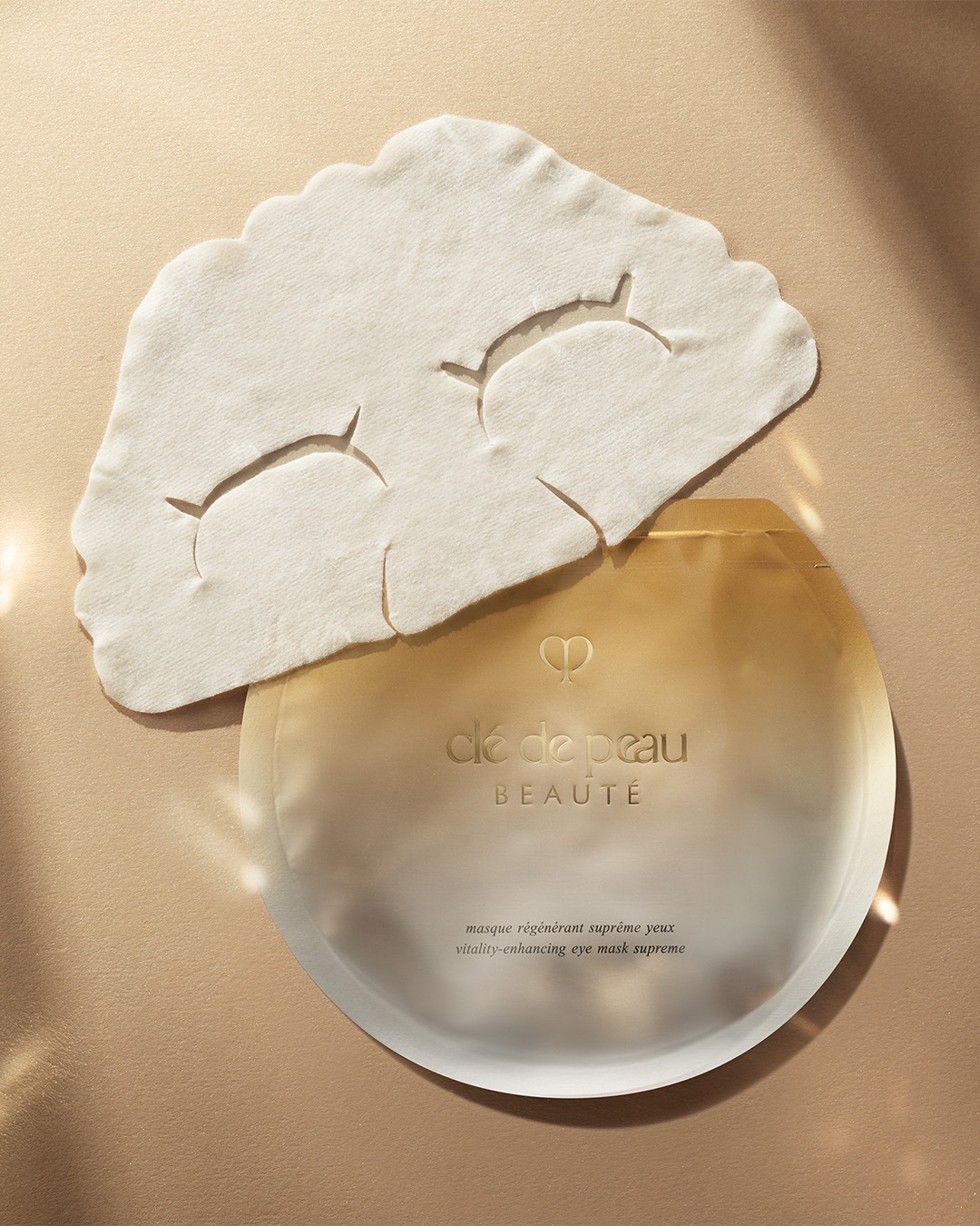 Die Clé de Peau Beauté Vitality-Enhancing Eye Mask Supreme ist eine Tuchmaske mit Aussparungen für die Augen, die in einer goldenen Verpackung geliefert wird.