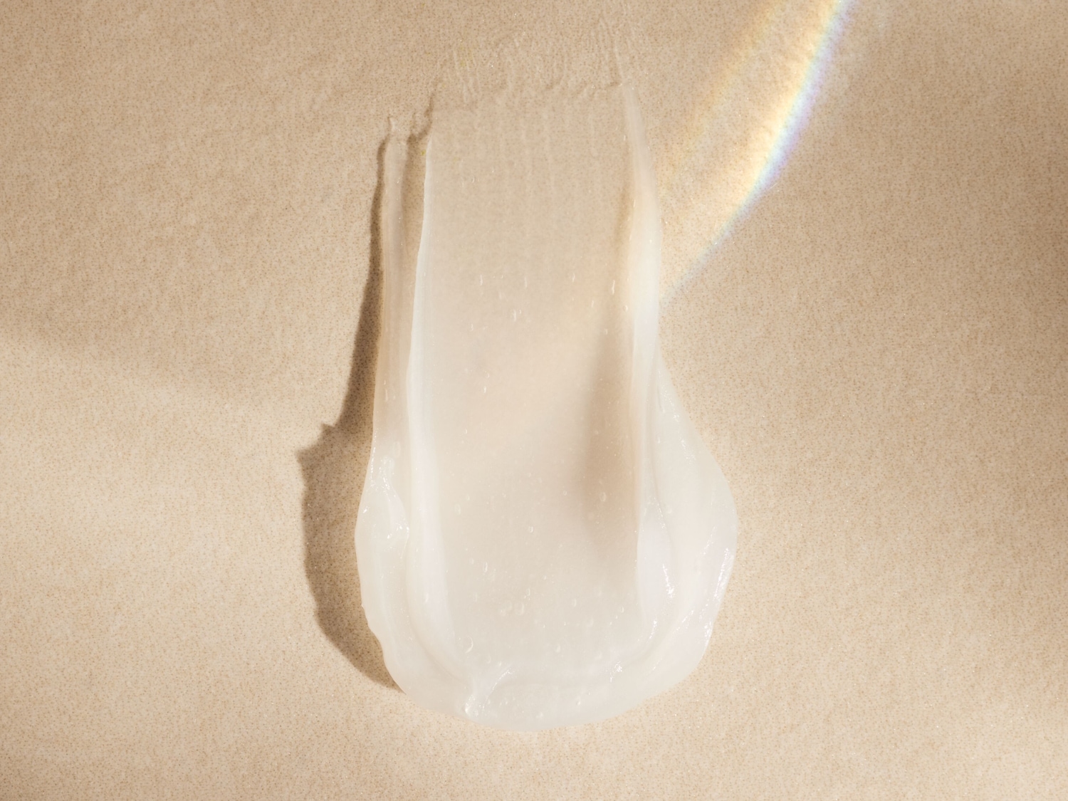 Ecco una texture liscia e traslucida di un prodotto di bellezza spalmato su una superficie beige, catturando la luce per una finitura luminosa.