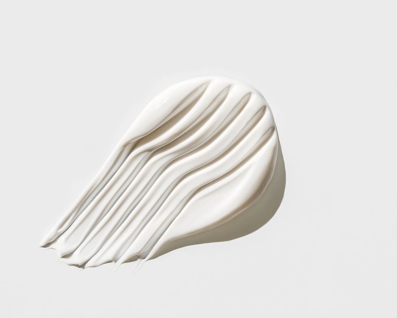 Detailní záběr na bílý krémový produkt s hladkou texturou, rozetřený na bílém pozadí, ideální pro péči o pleť.