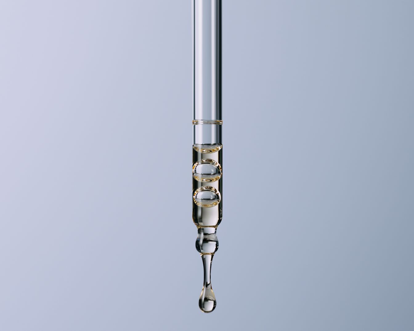 Primo piano di un contagocce trasparente pieno di liquido dorato, con bolle visibili all'interno, su sfondo azzurro.